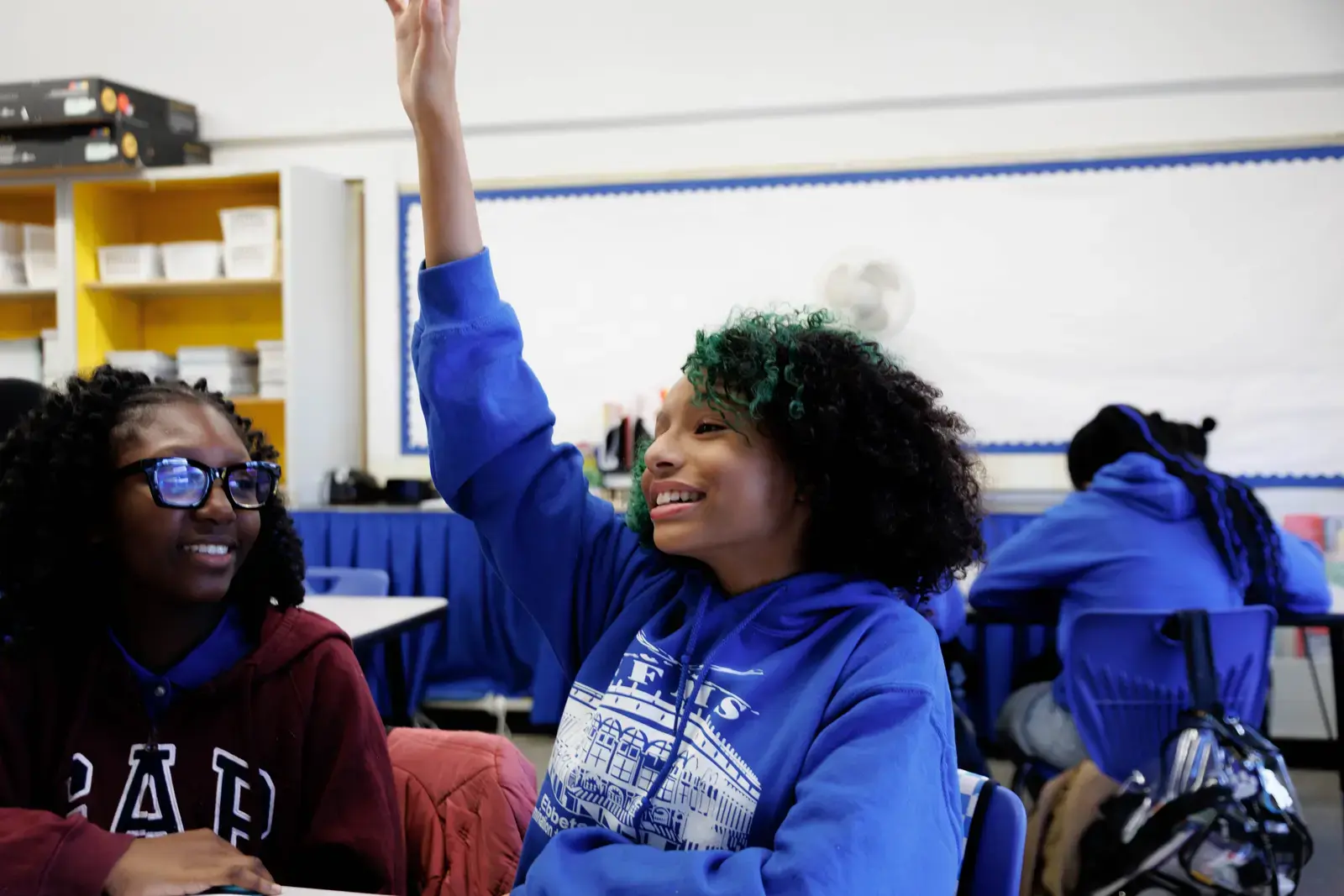 Student raising hand enthusiastically in a middle school classroom