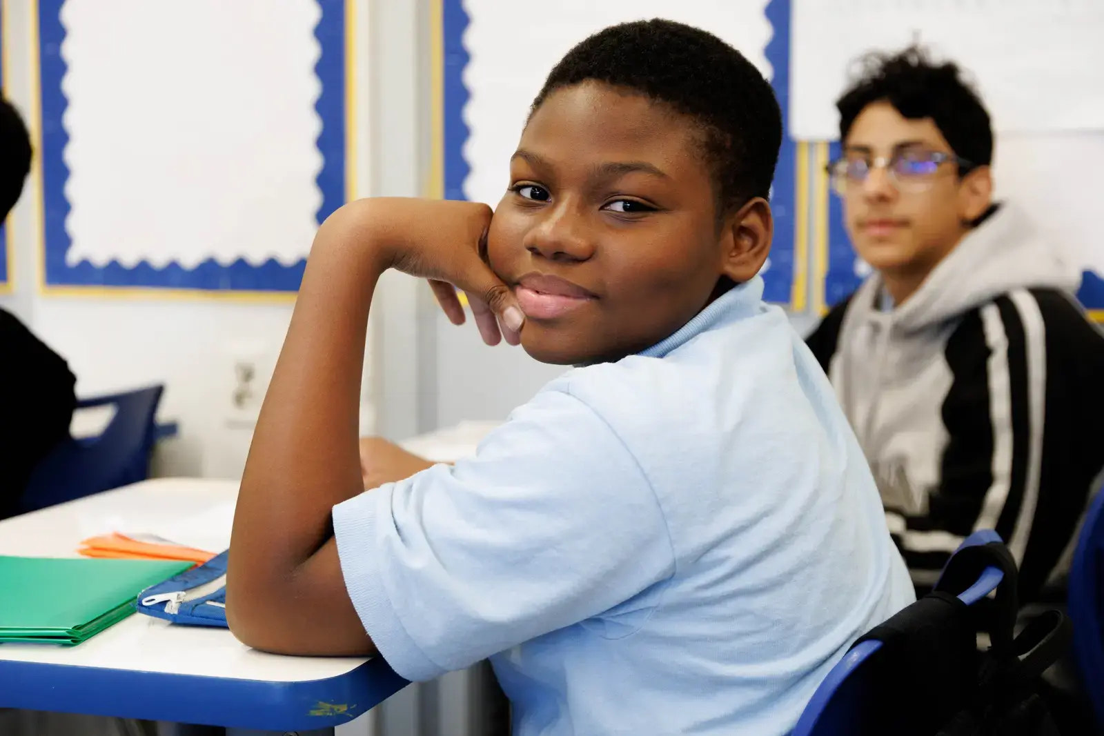 Smiling middle school student seated at classroom desk with folders