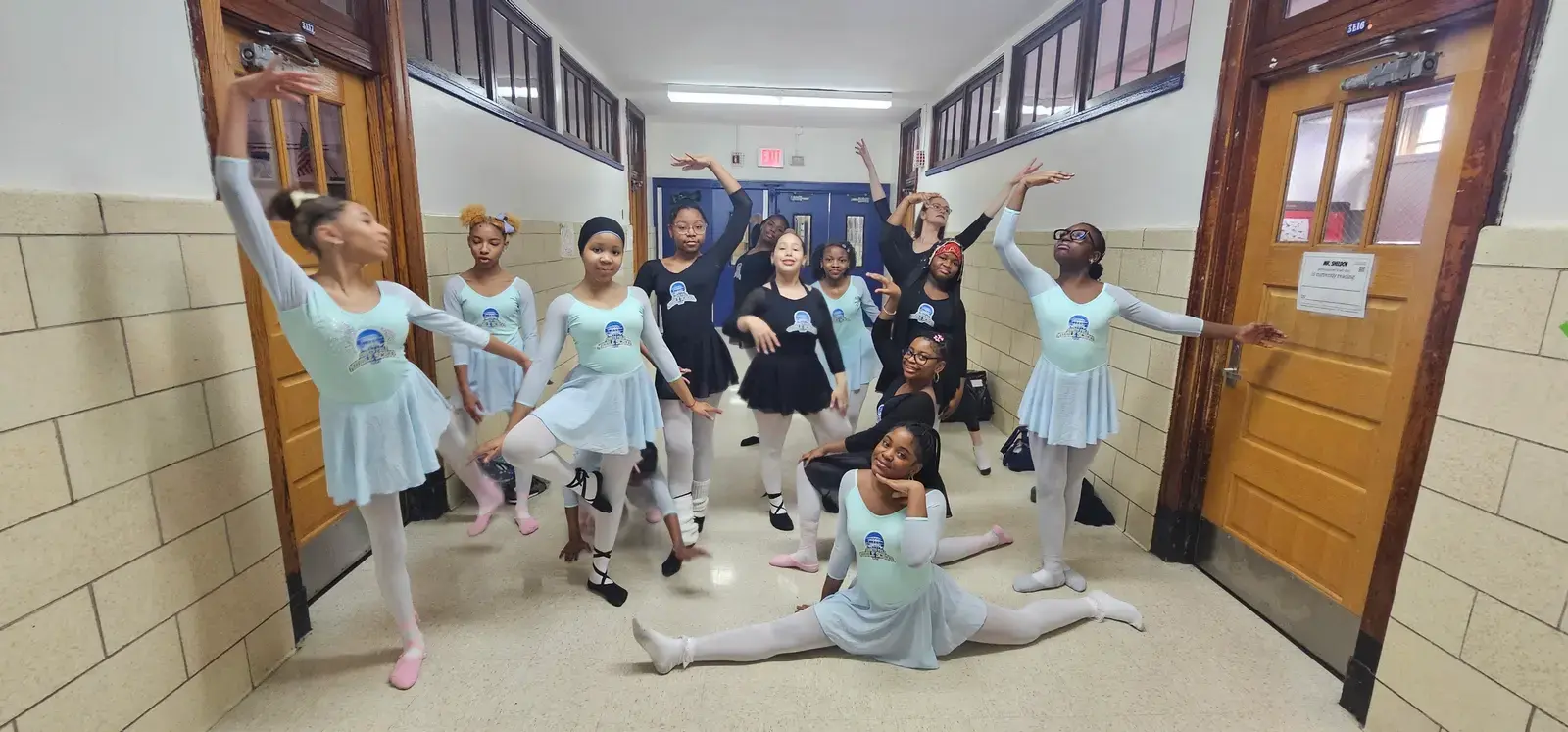 Student ballet dancers posing in school hallway in matching costumes