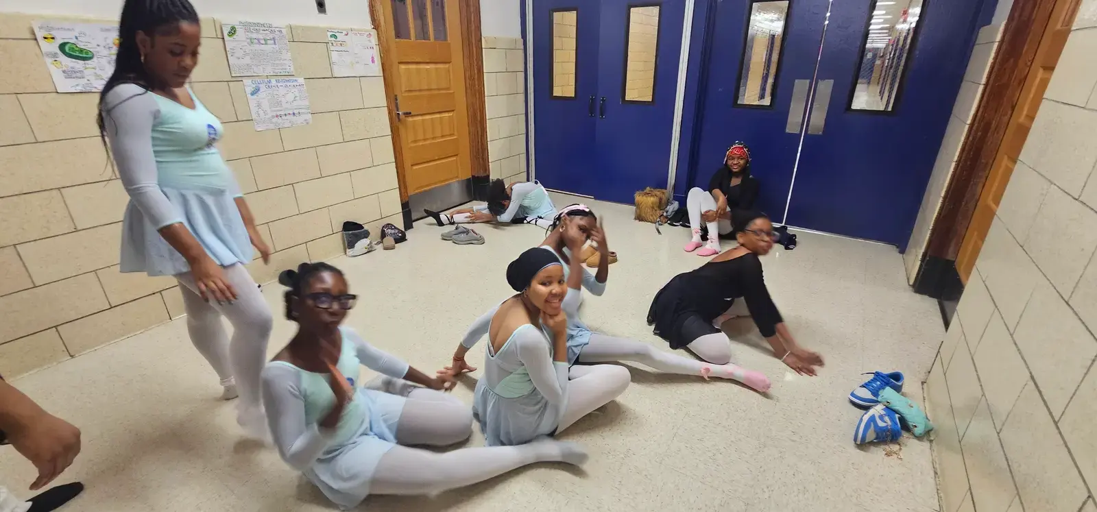 Student dancers in blue costumes stretching in school hallway before performance