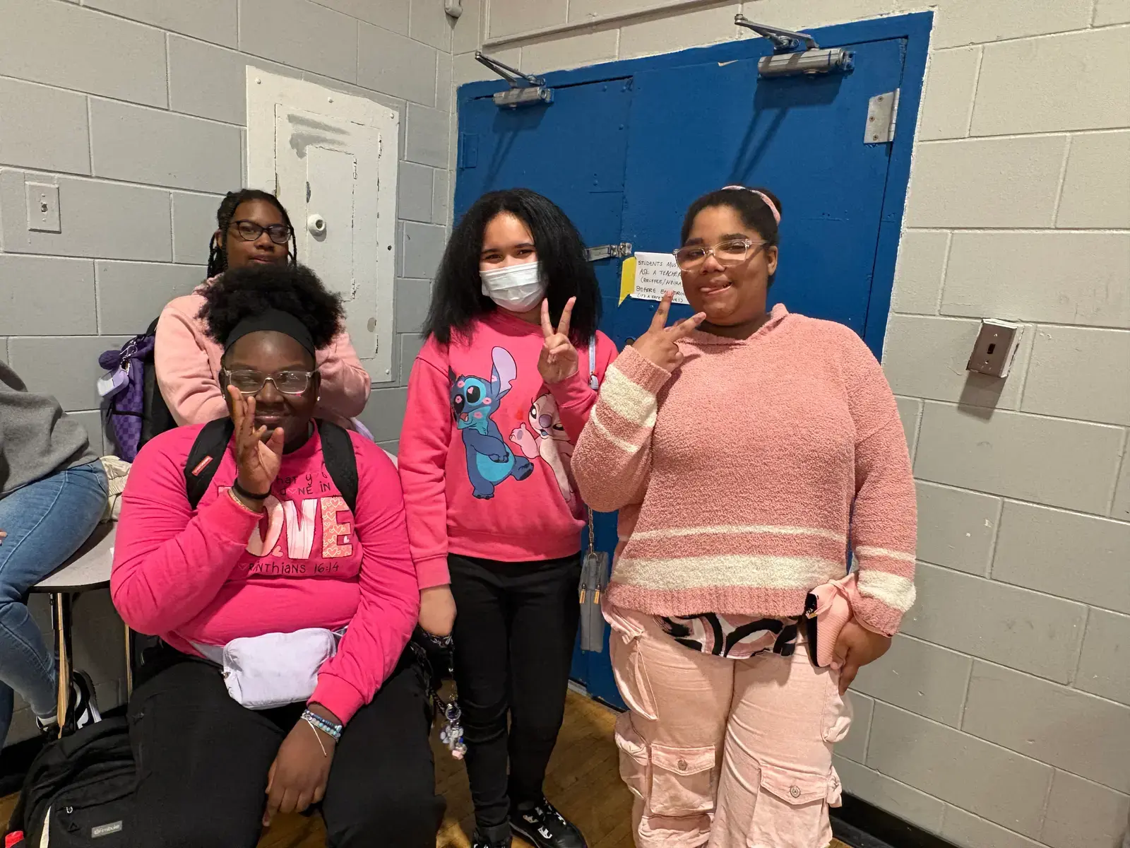 Four students wearing pink posing together in a classroom