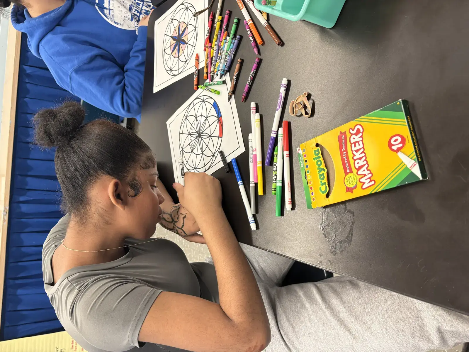 Student coloring a mandala worksheet with markers and crayons