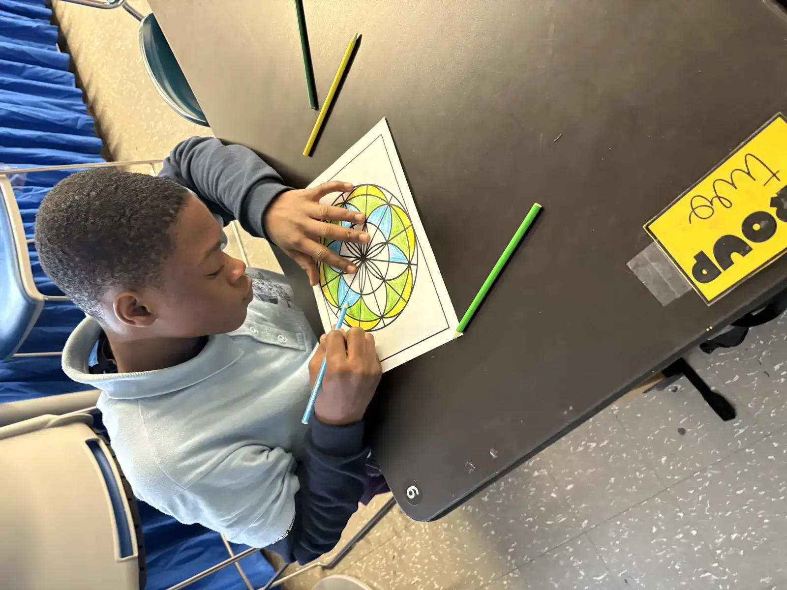Student coloring a geometric mandala design at classroom desk