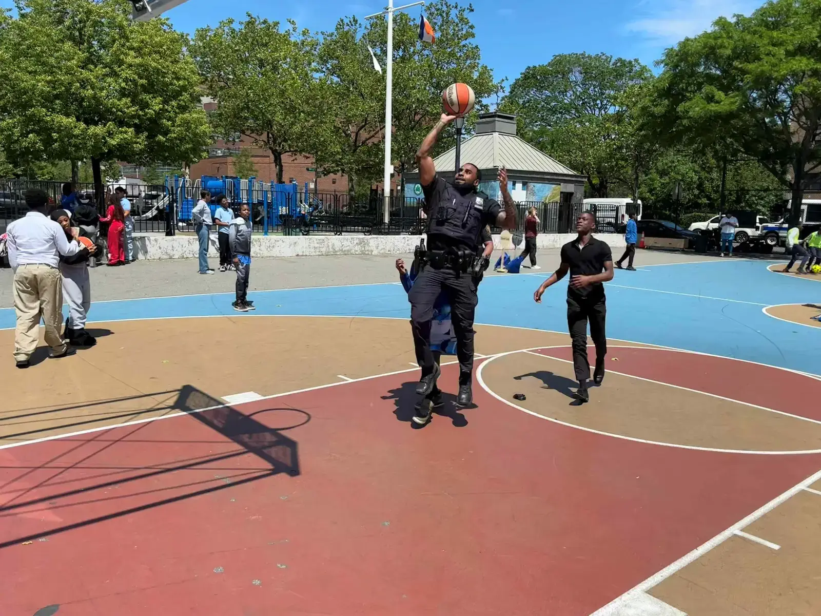 Police officer shooting a basketball on an outdoor court with students nearby