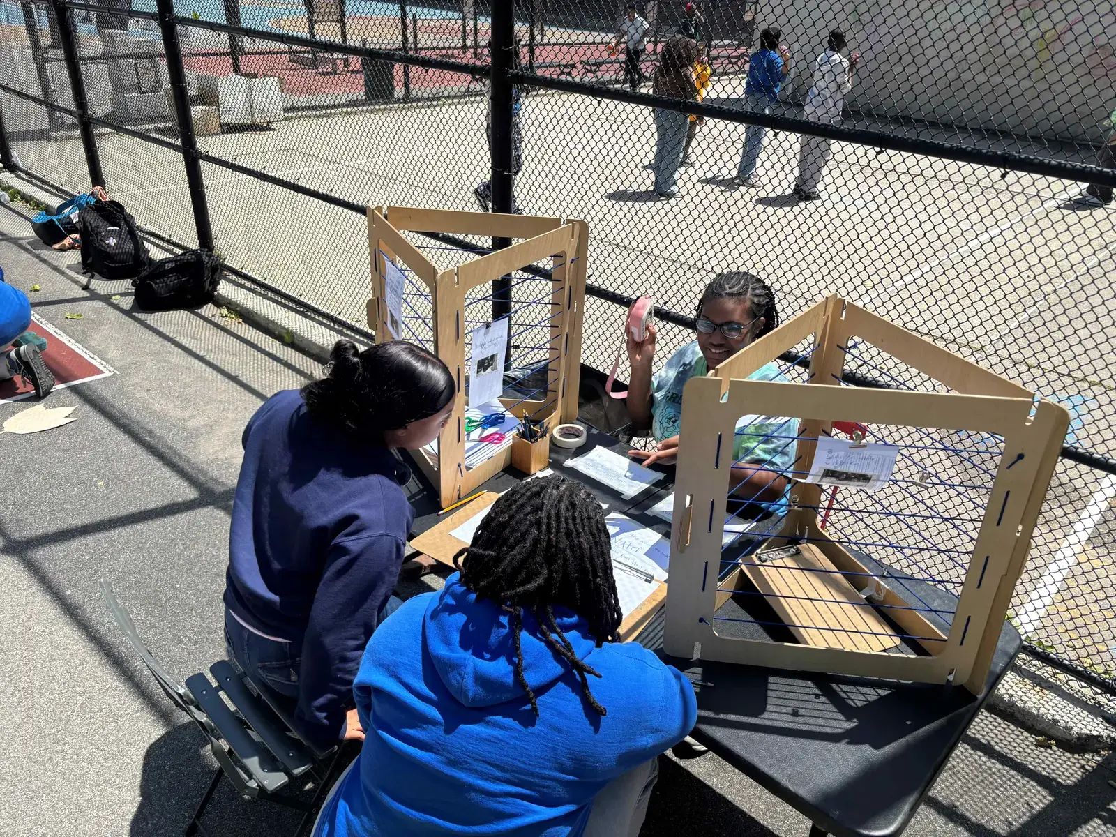 Students working with wooden loom frames at outdoor table activity