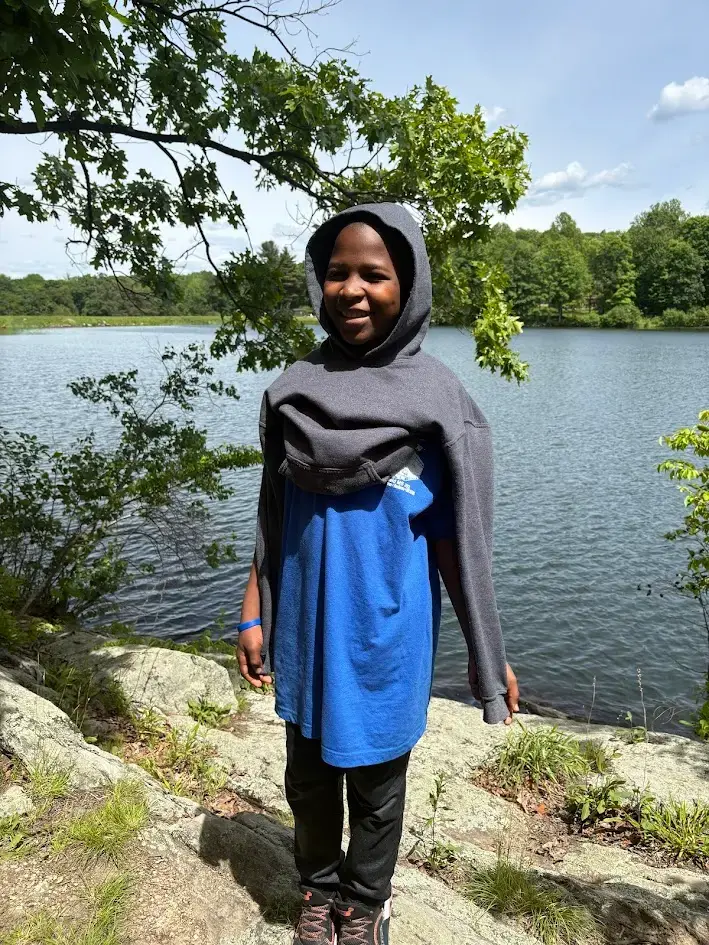 Student smiling outdoors near a lake during a school trip