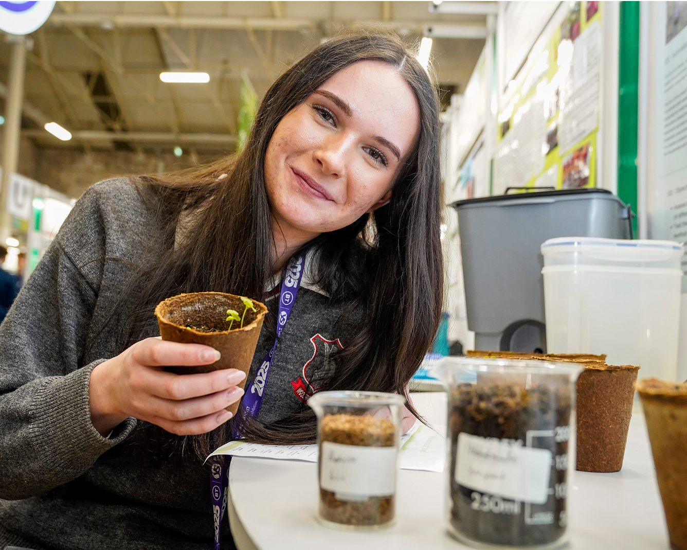 Student smiling while holding a small plant pot at a science exhibition.