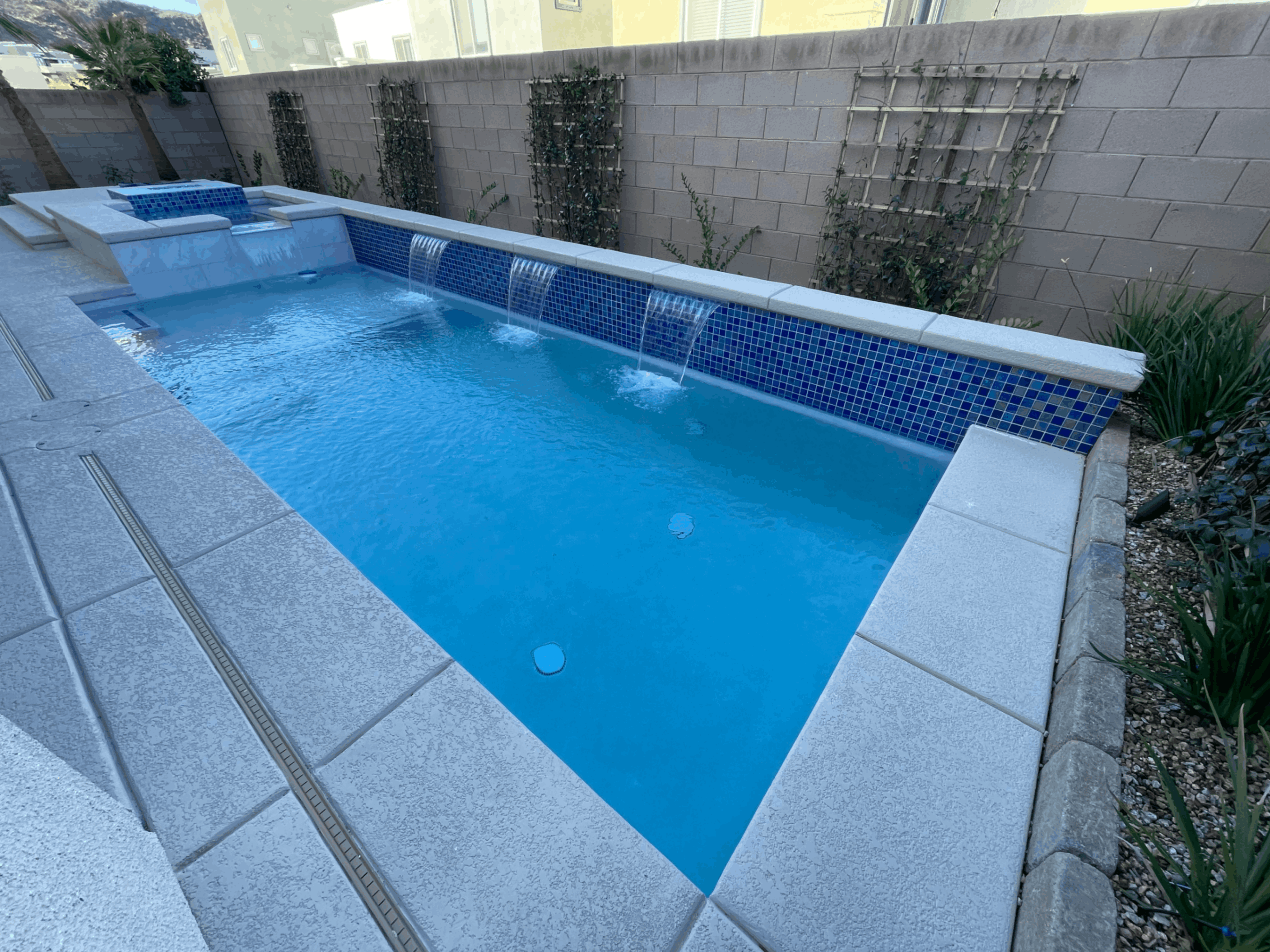Daytime view of a sleek backyard pool with granite edging and minimalist landscaping