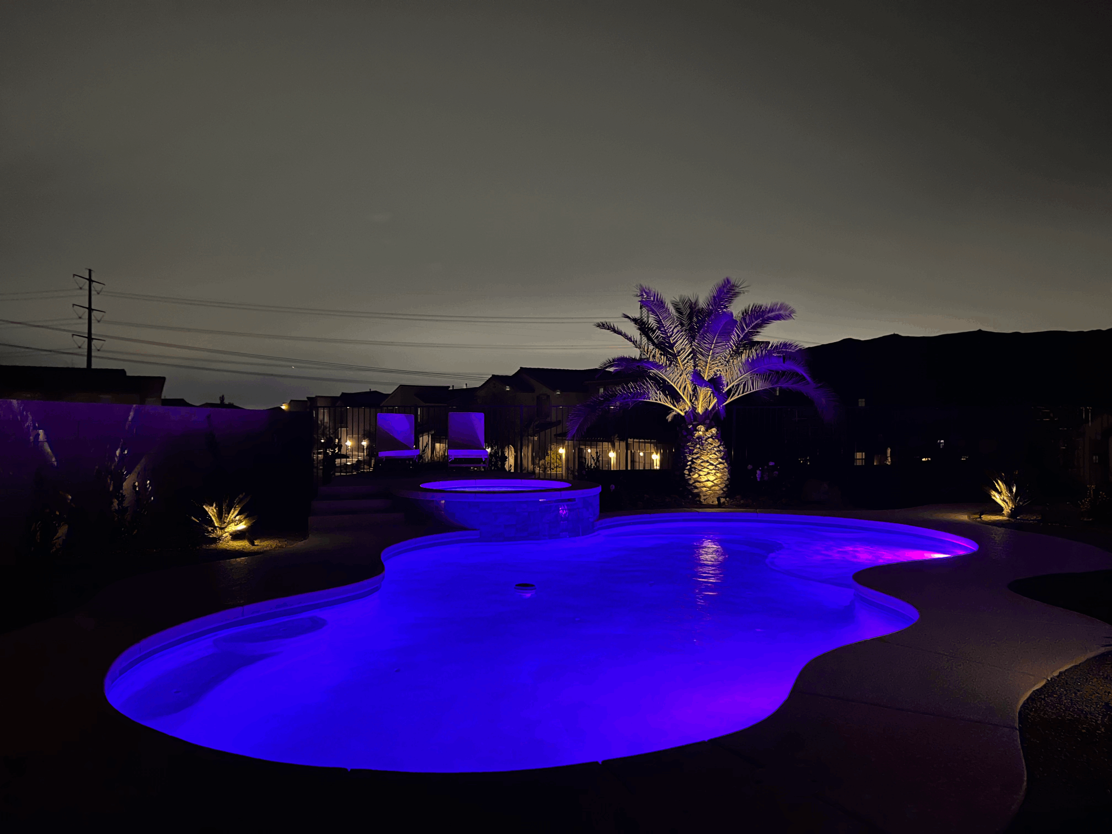 Illuminated pool and spa at night with cascading water features and ambient lighting