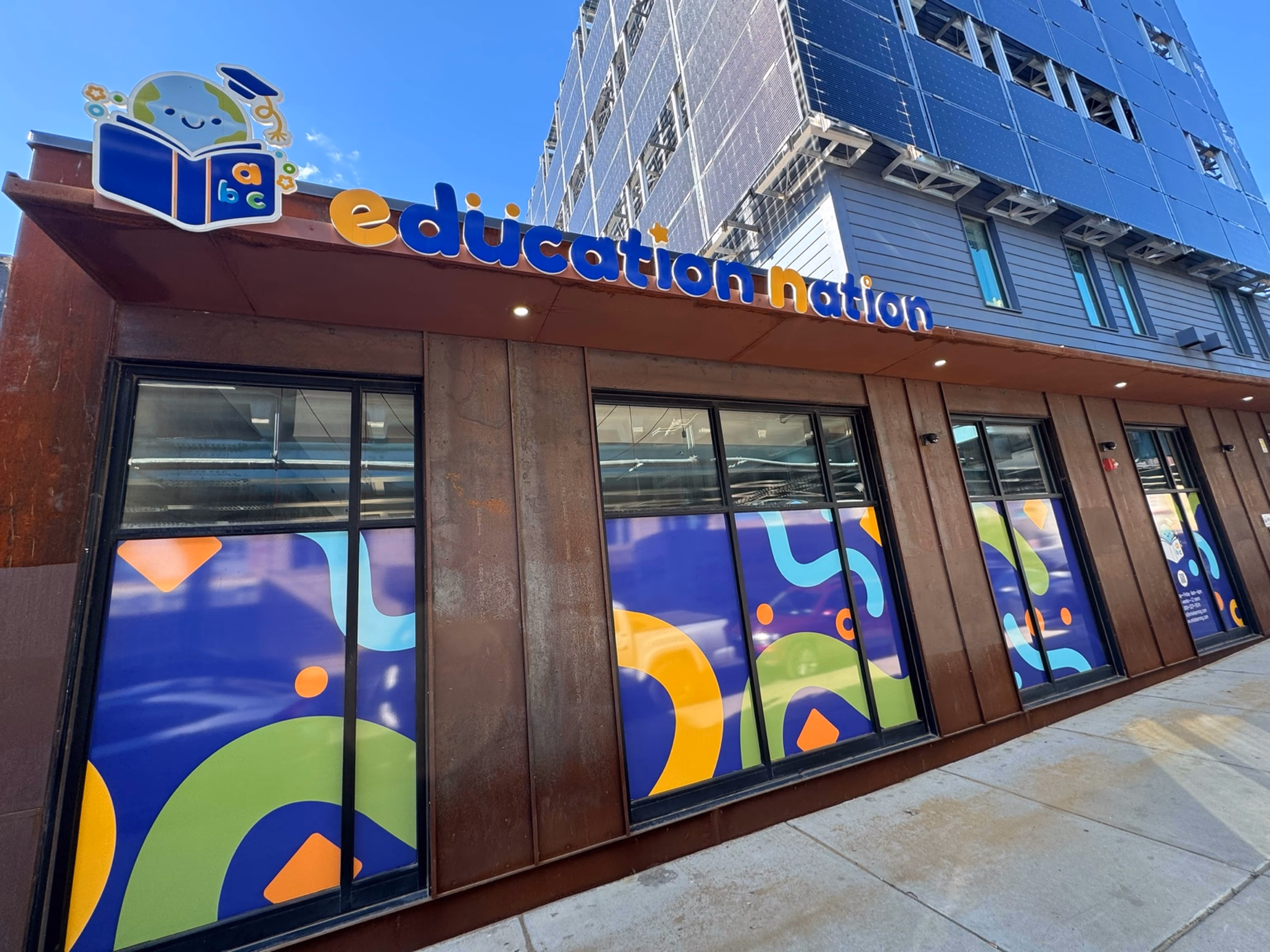 Exterior of a building with large colorful windows and a sign reading 'education nation' featuring a smiling globe with a graduation cap reading ABC.