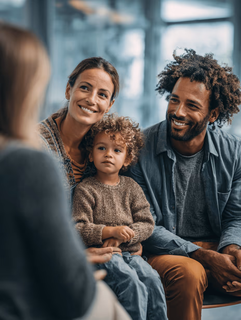 Smiling parents sitting with their young child on mother's lap during a conversation.