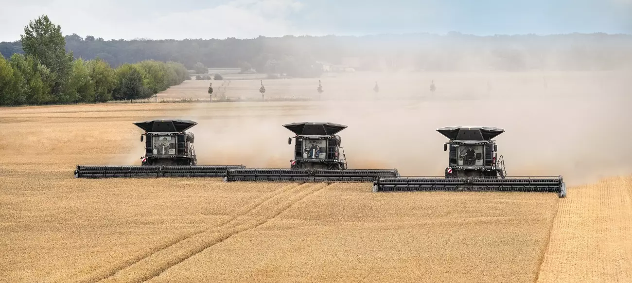 3 large farm machinery headers in a wheat field