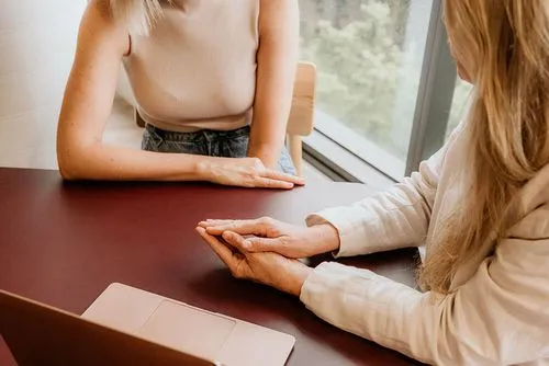 Two women sitting at a table with a laptop.