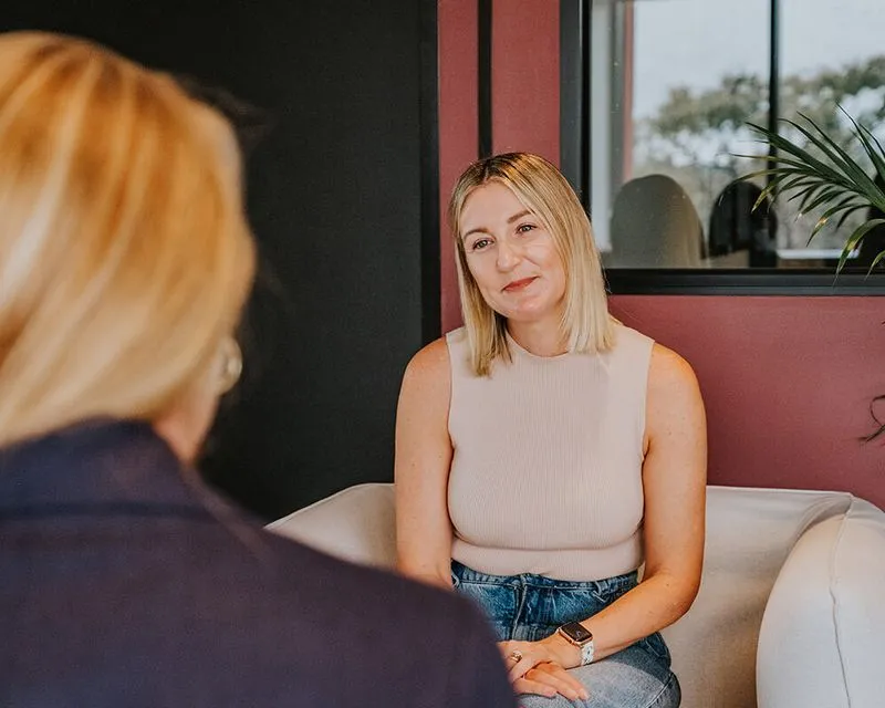 A woman sitting on a couch talking to another woman.