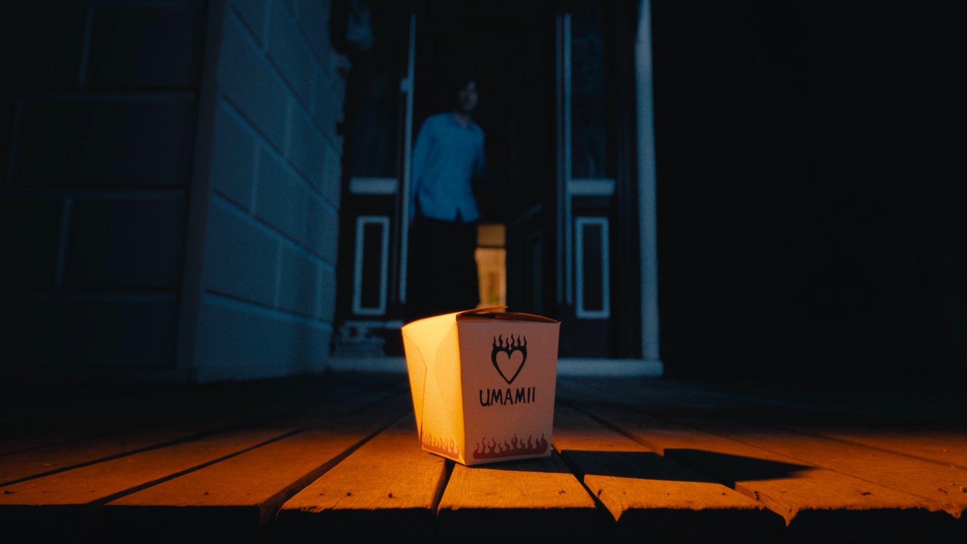 A noodle box sitting on a dimly lit porch at night. A man is standing in the doorway looking at the noodles.