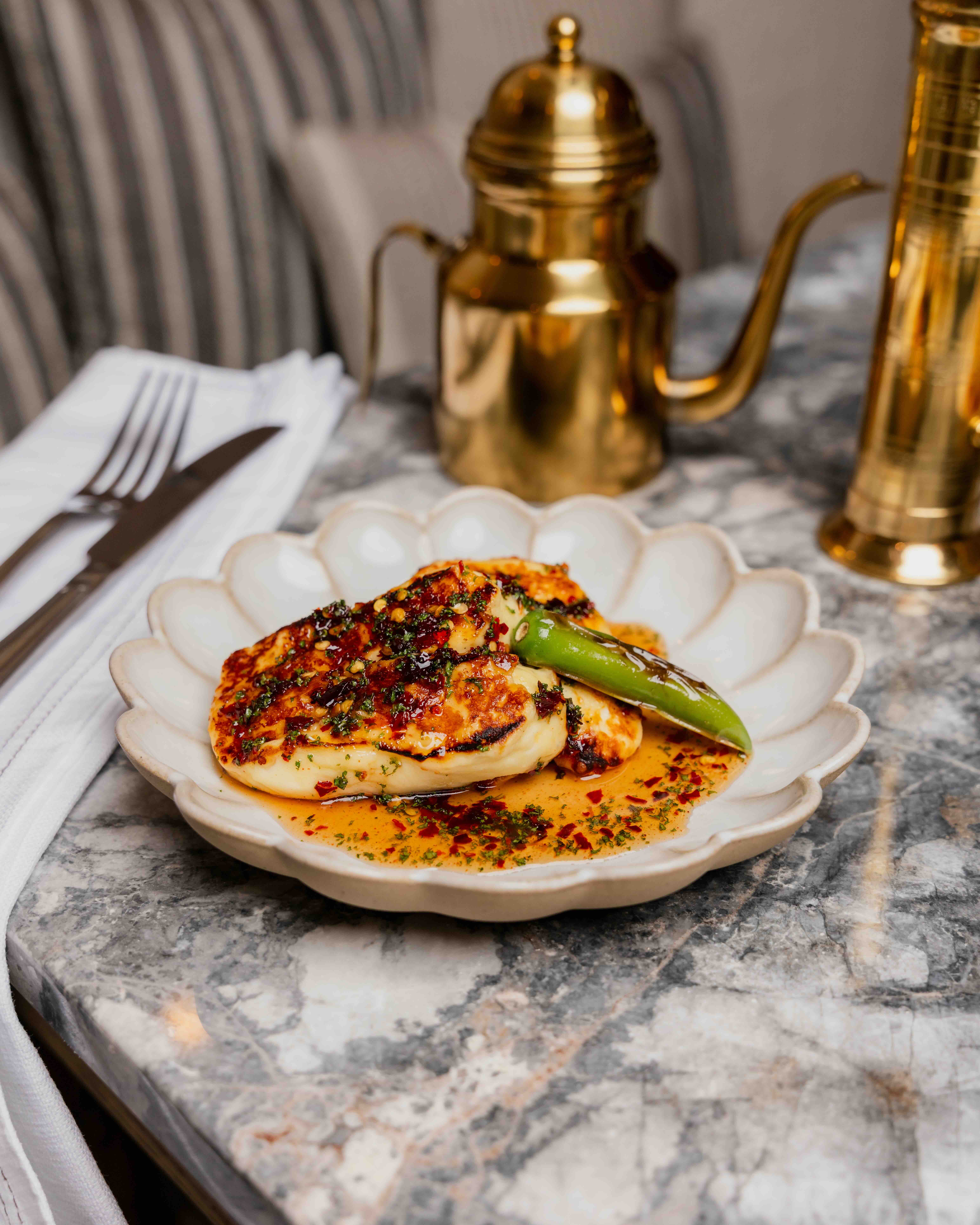 Plate with grilled cheese covered in spices and sauce, garnished with a whole green chili pepper.