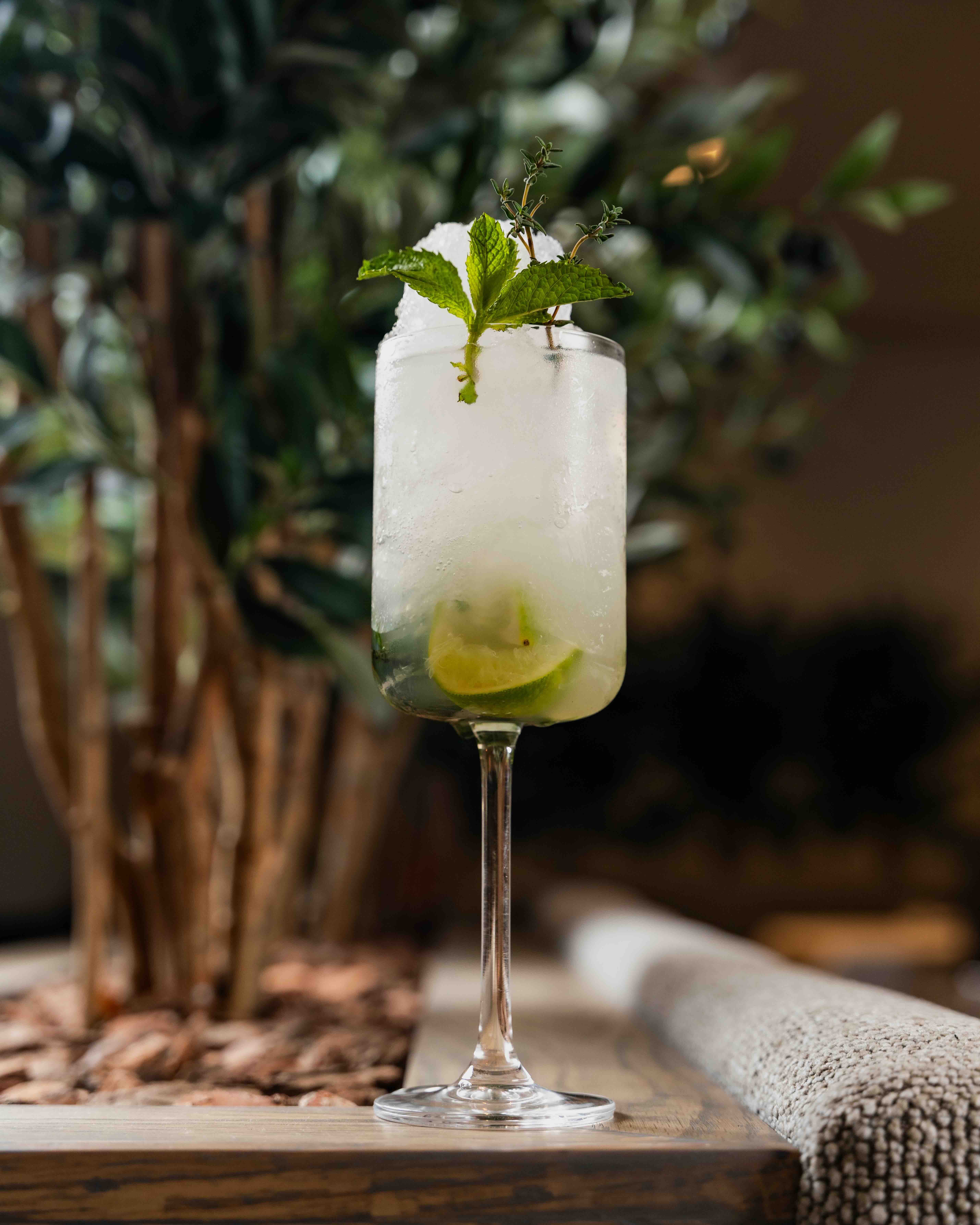 Tall glass with crushed ice, lime wedges, and mint leaves on a wooden table.