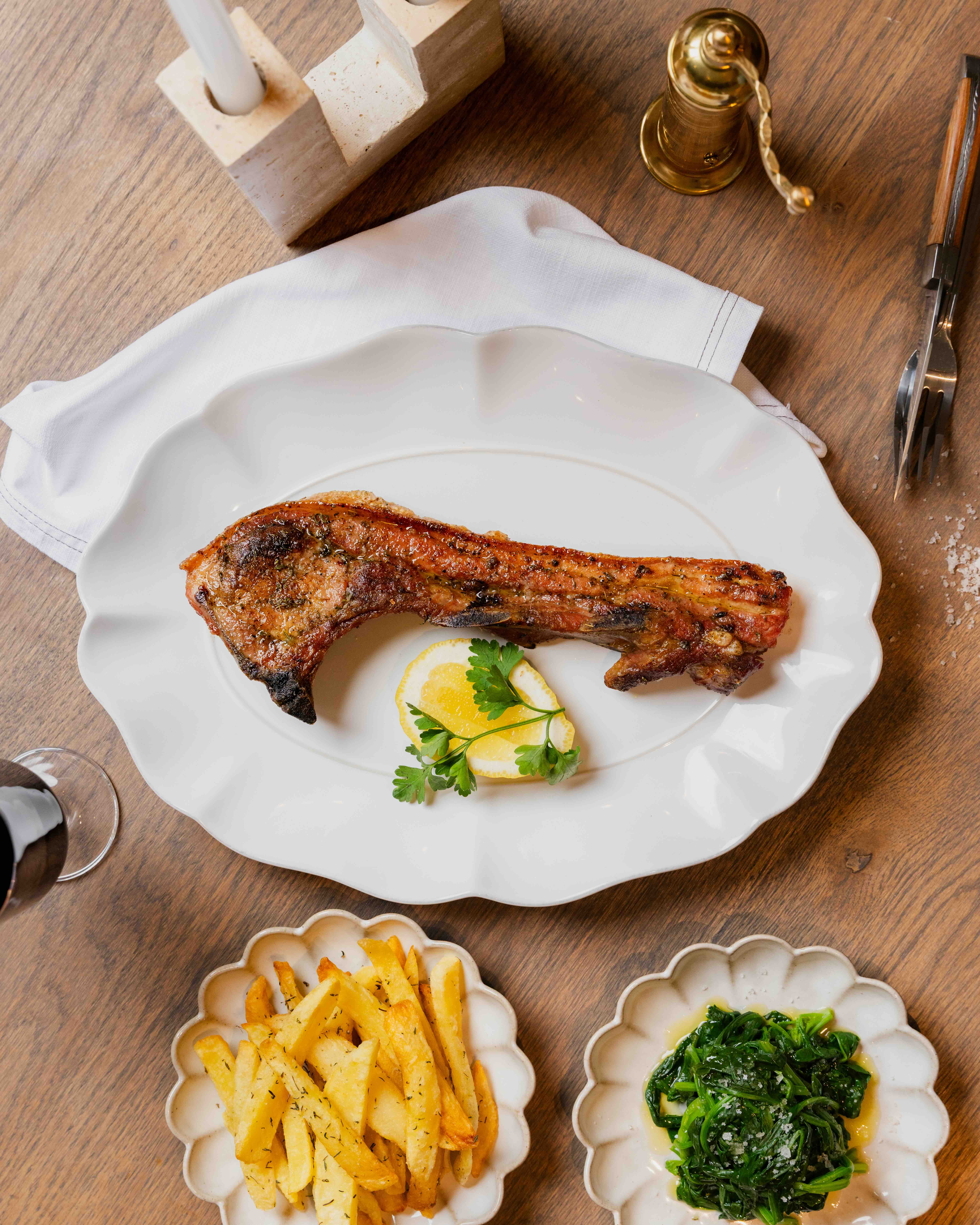 Grilled pork chop on white plate with lemon slice and parsley, served with fries and sautéed greens.