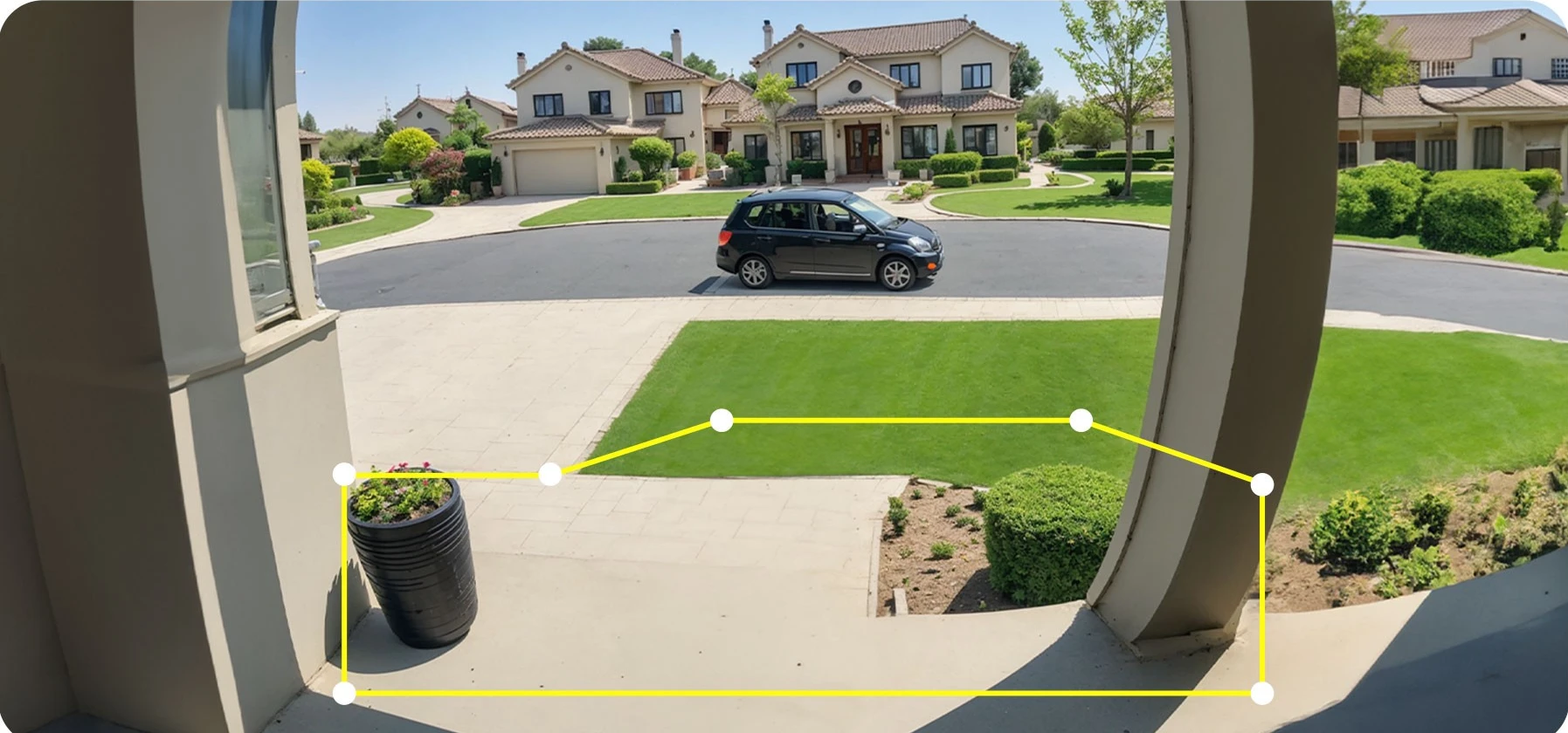 View from a porch with a black planter on the left, overlooking a street with a parked black car and houses with tiled roofs in the background.