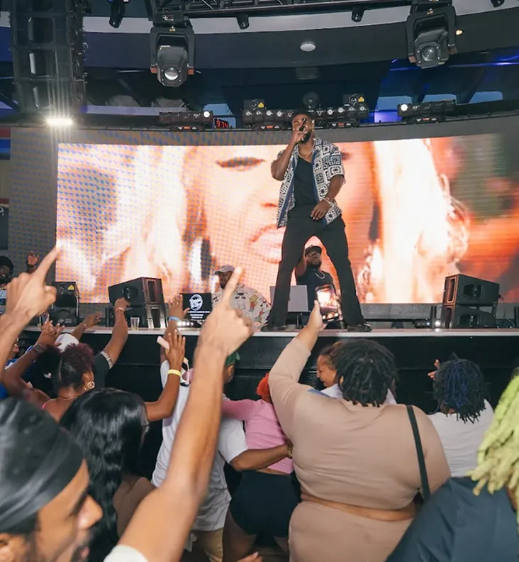 Performer on stage hyping a crowd with a large screen backdrop.