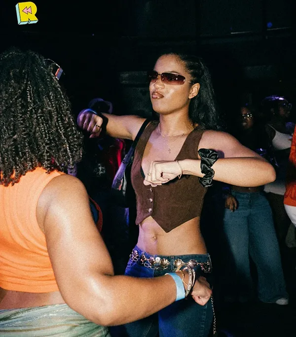 Two women dancing together at a packed club, one wearing sunglasses and a crop top.