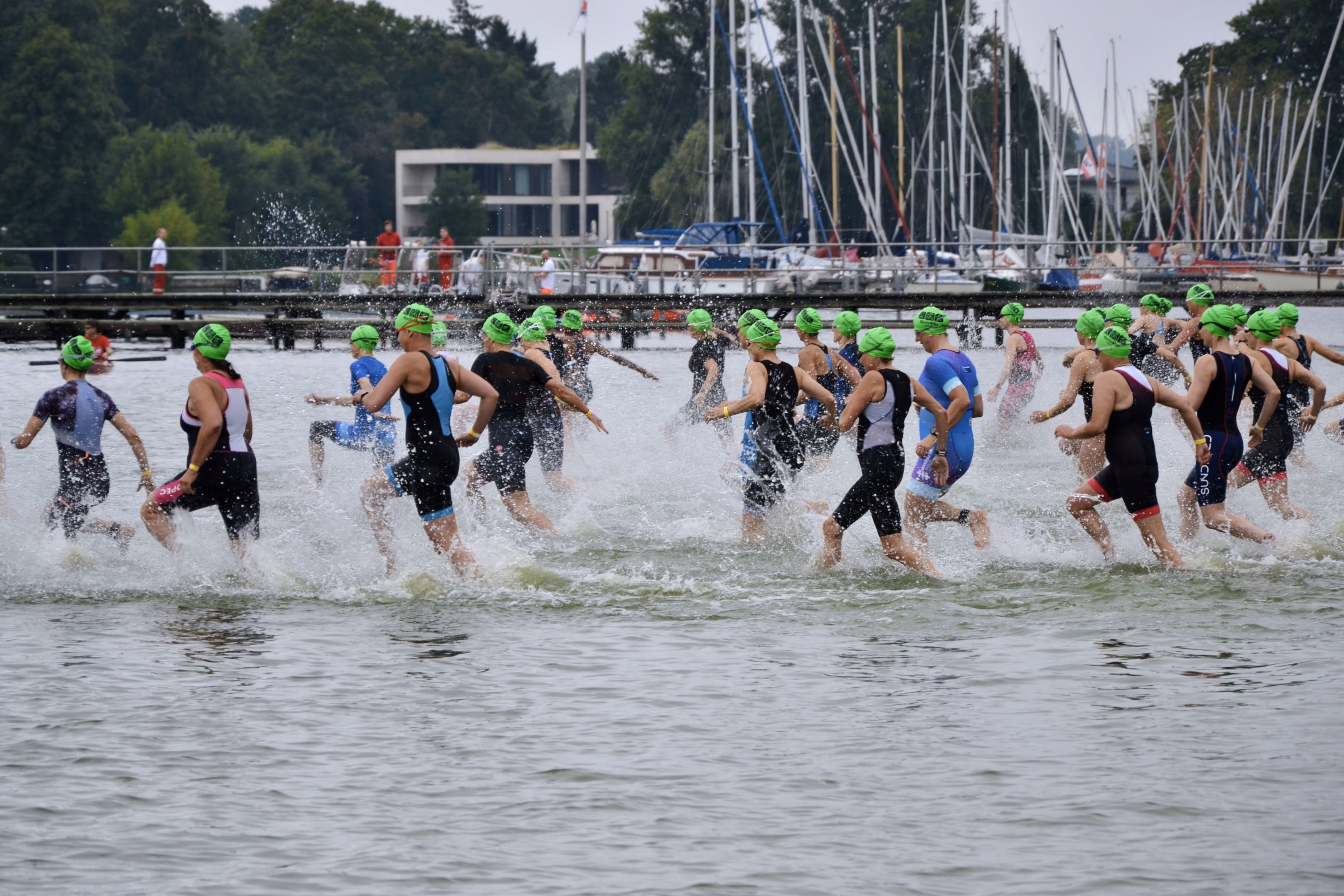 Triathlet*innen mit grünen Badekappen rennen beim BerlinWoMan Triathlon ins Wasser des Wannsees.