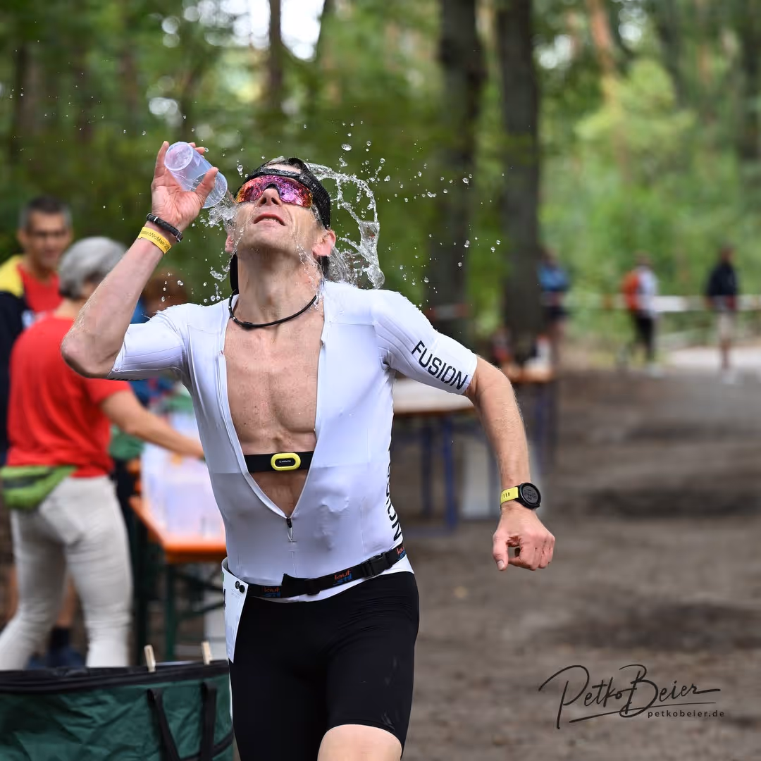 Triathlet gießt sich während eines Wettlaufs Wasser über den Kopf im Wald.