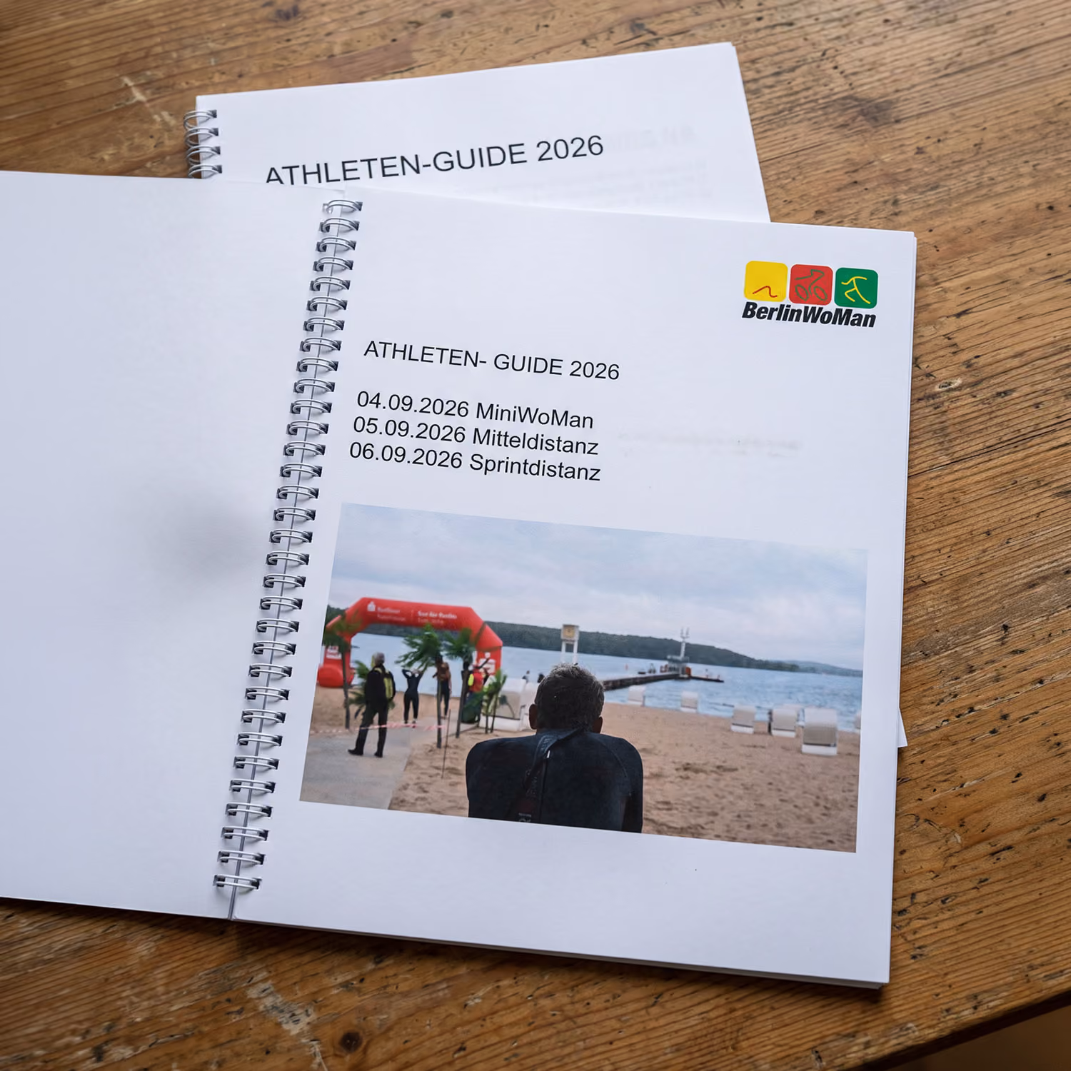 Aufgeklappter Athleten-Guide 2026 mit Veranstaltungsterminen und Foto eines Strandes mit Personen vor einer Wasserstrecke.