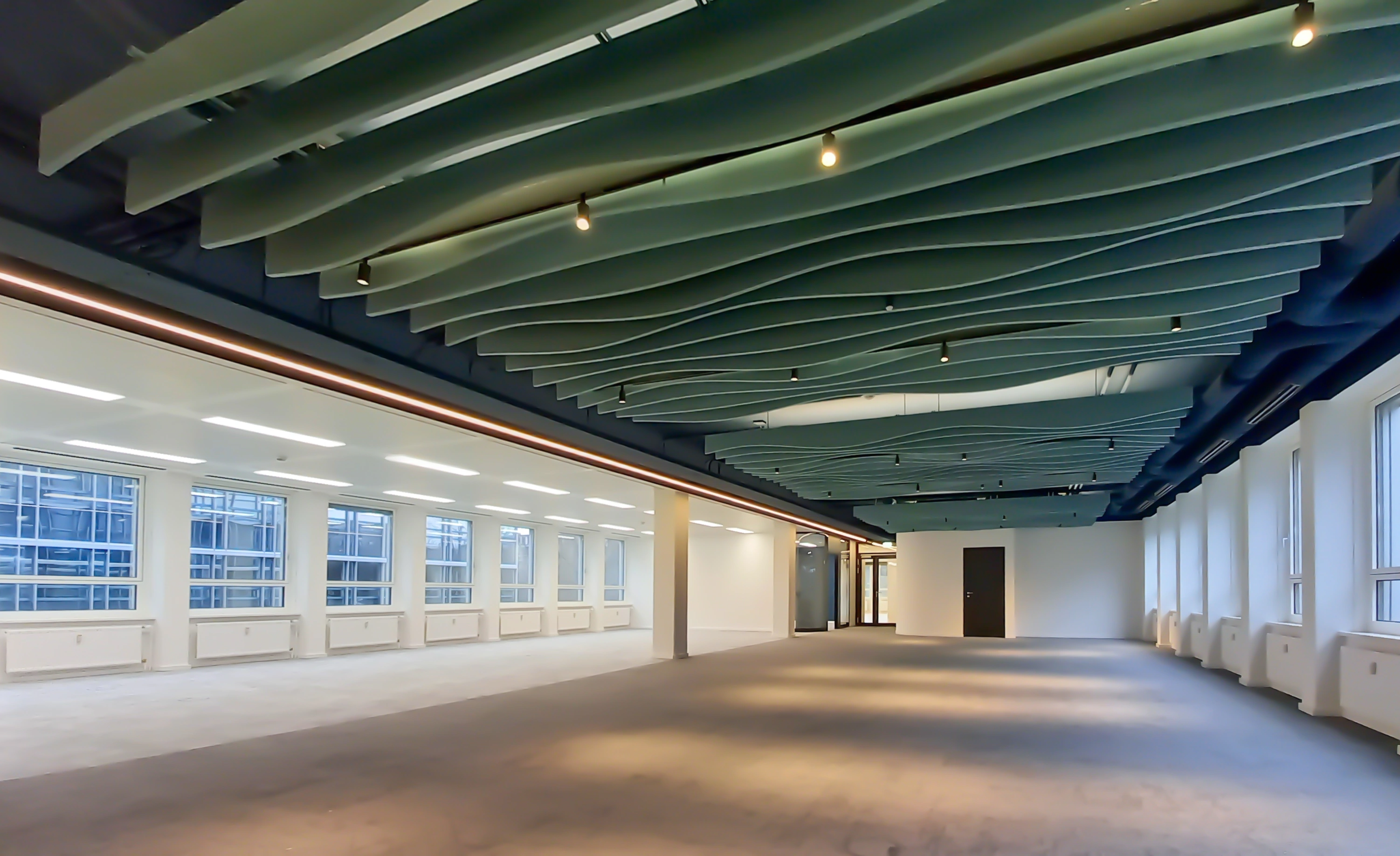 A spacious industrial-style hall with a green ceiling structure and floor-to-ceiling windows.
