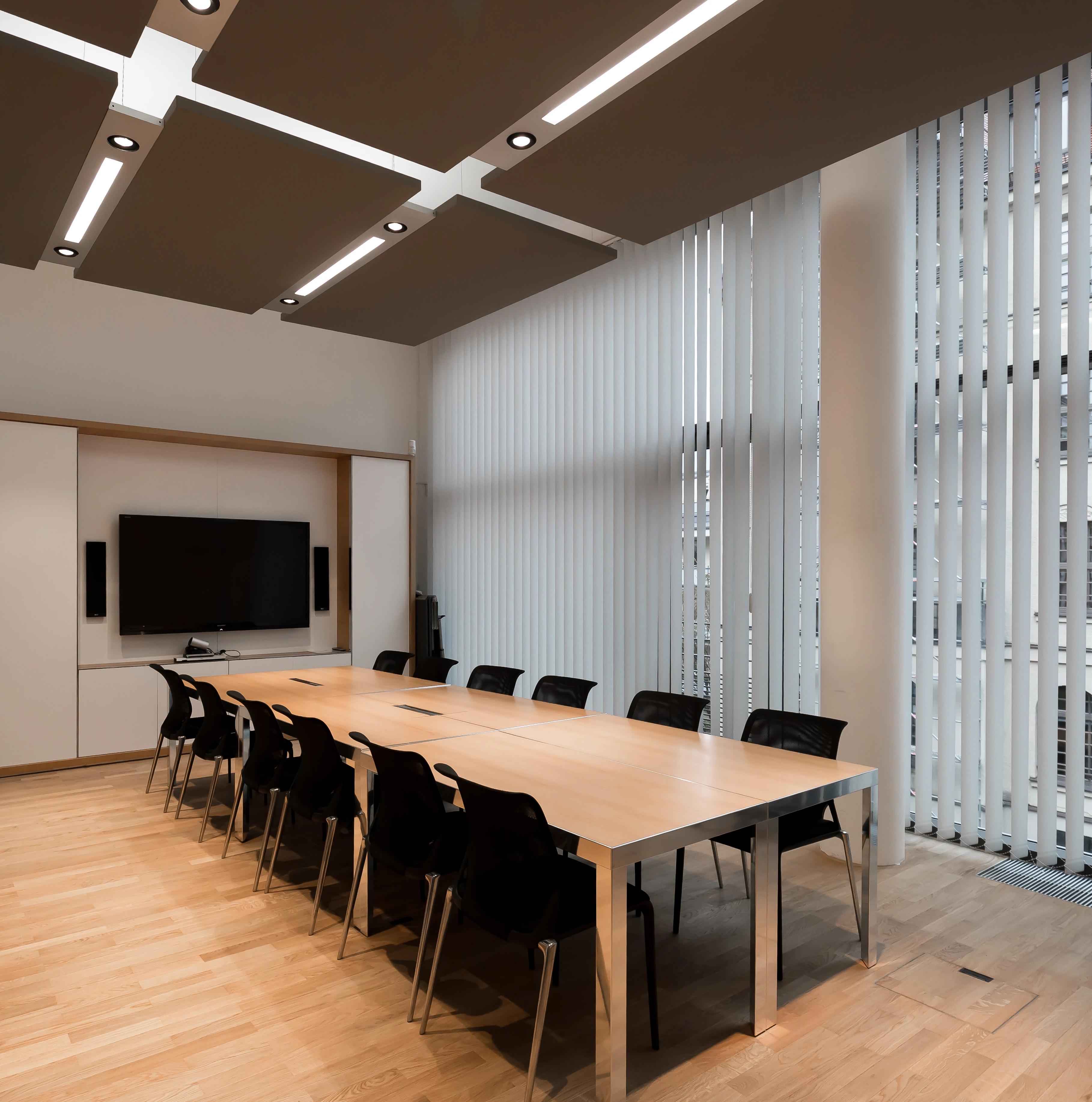 A meeting room with a long black table, dark ceiling panels, and floor-to-ceiling windows.