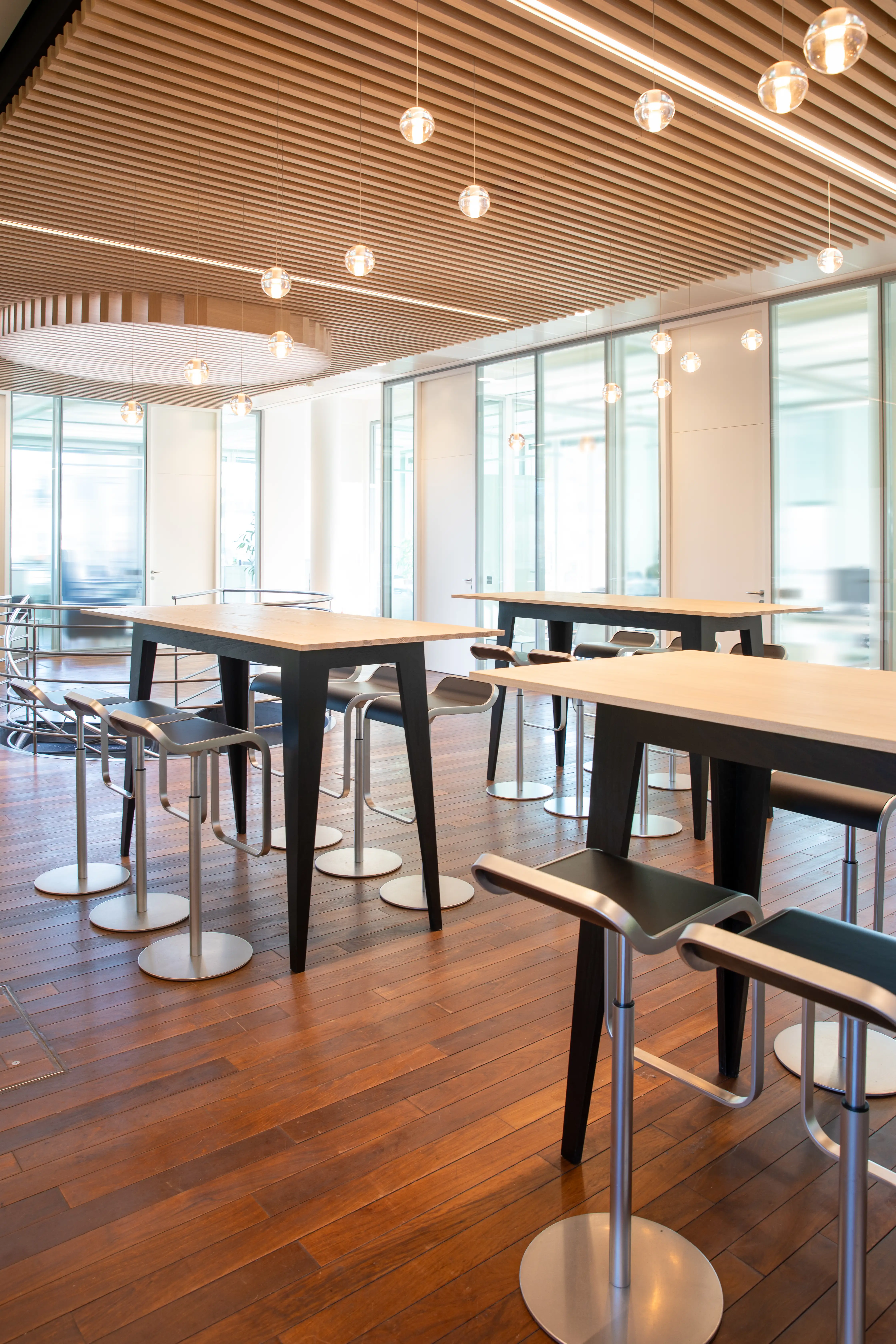 A bright cafeteria-style area with tall tables, bar stools, and a wooden slatted ceiling.