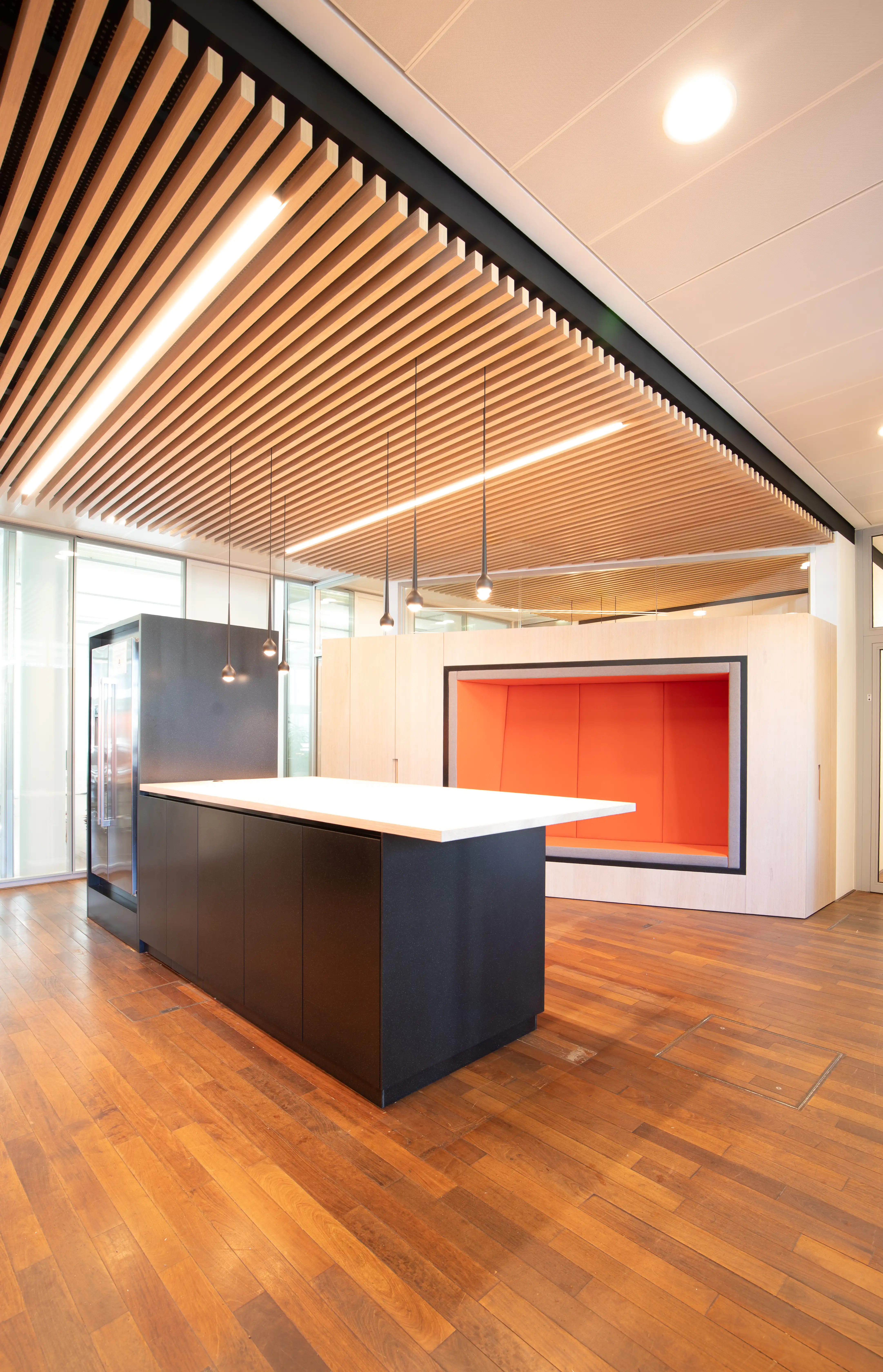 A contemporary office kitchen area with wood flooring, black cabinetry, and a bold red accent wall.