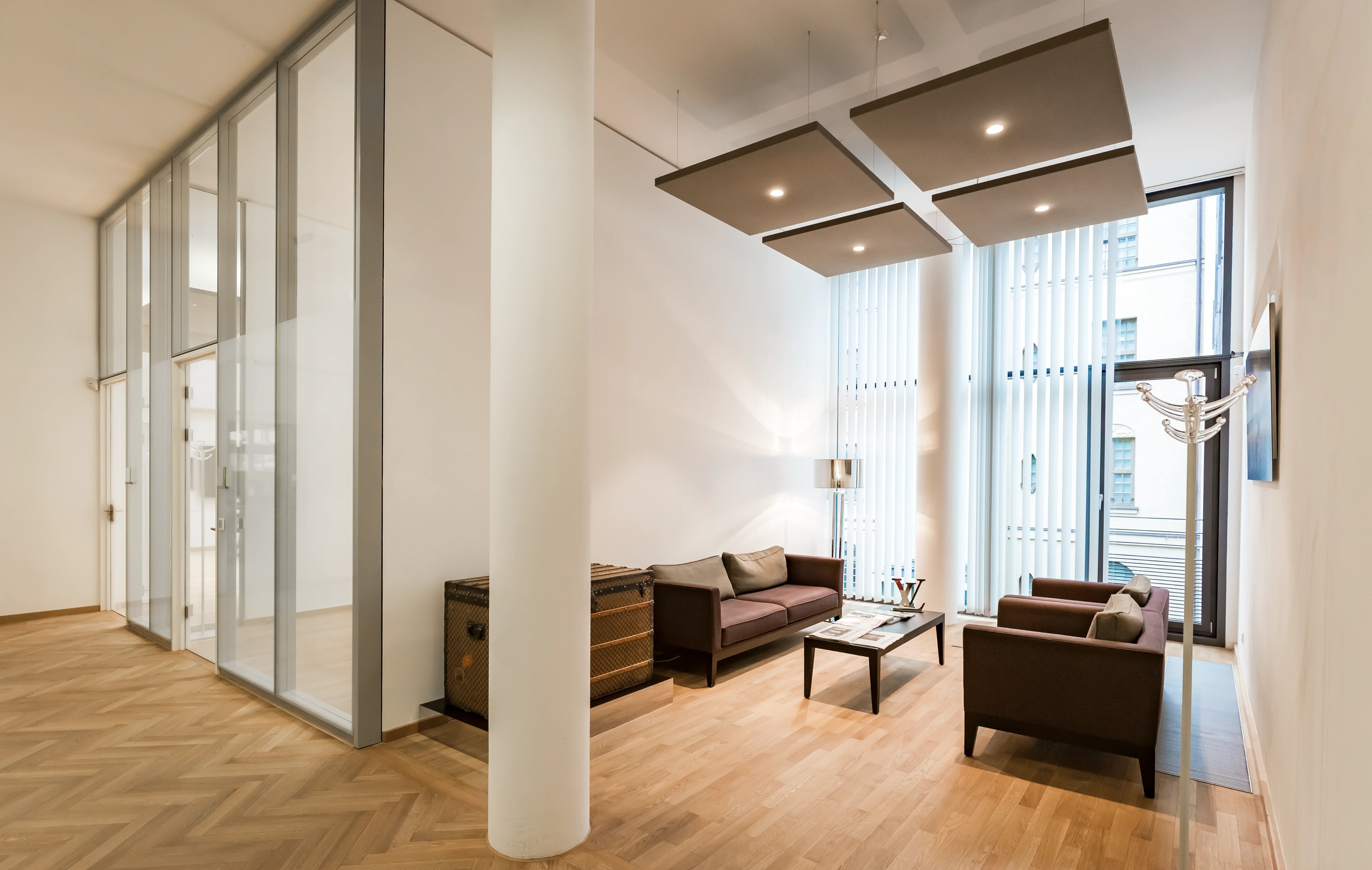 A bright office lounge with glass partitions, cozy armchairs, and natural light.