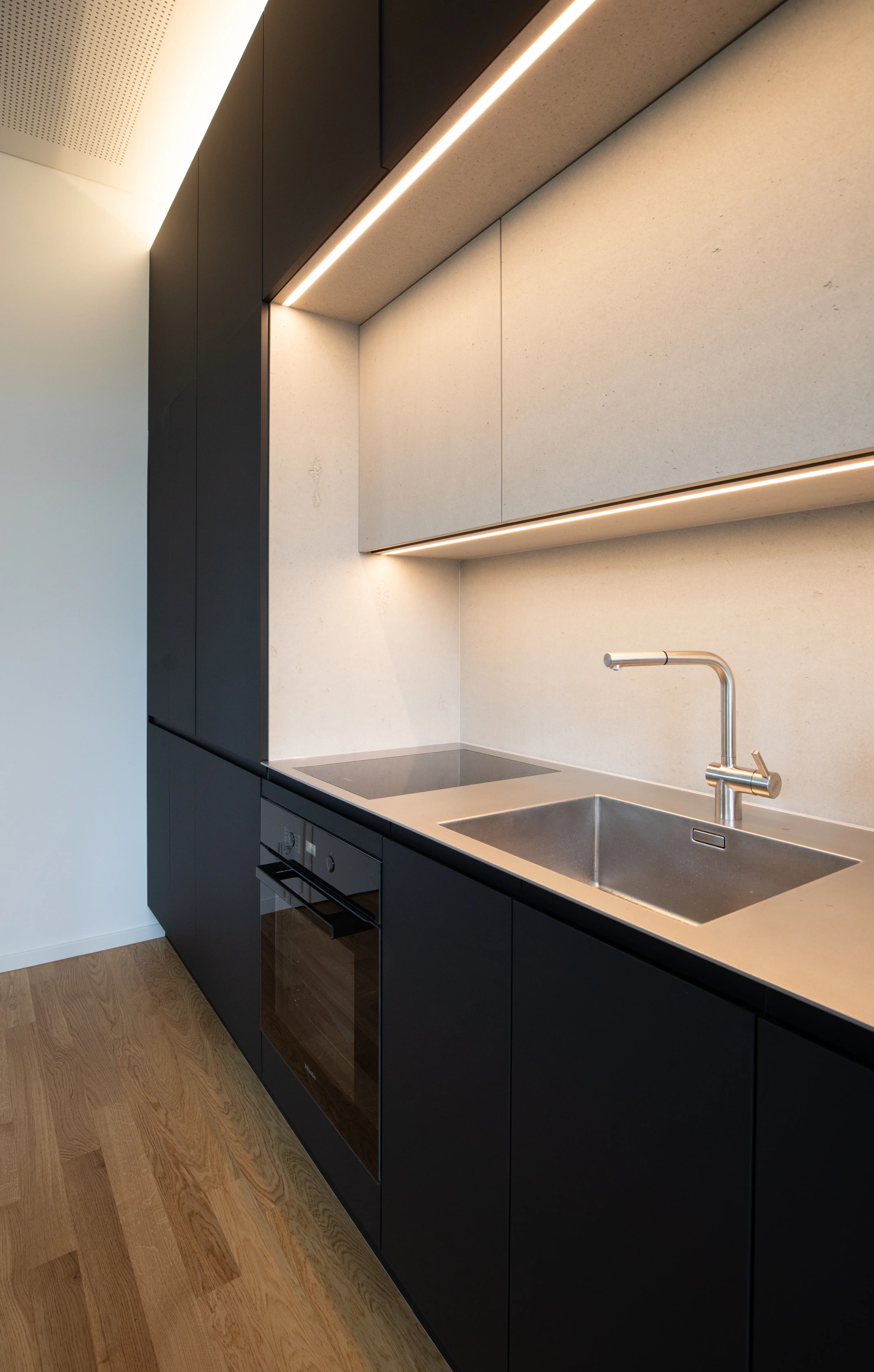 A contemporary kitchenette with black cabinetry, wood accents, and soft ambient lighting.