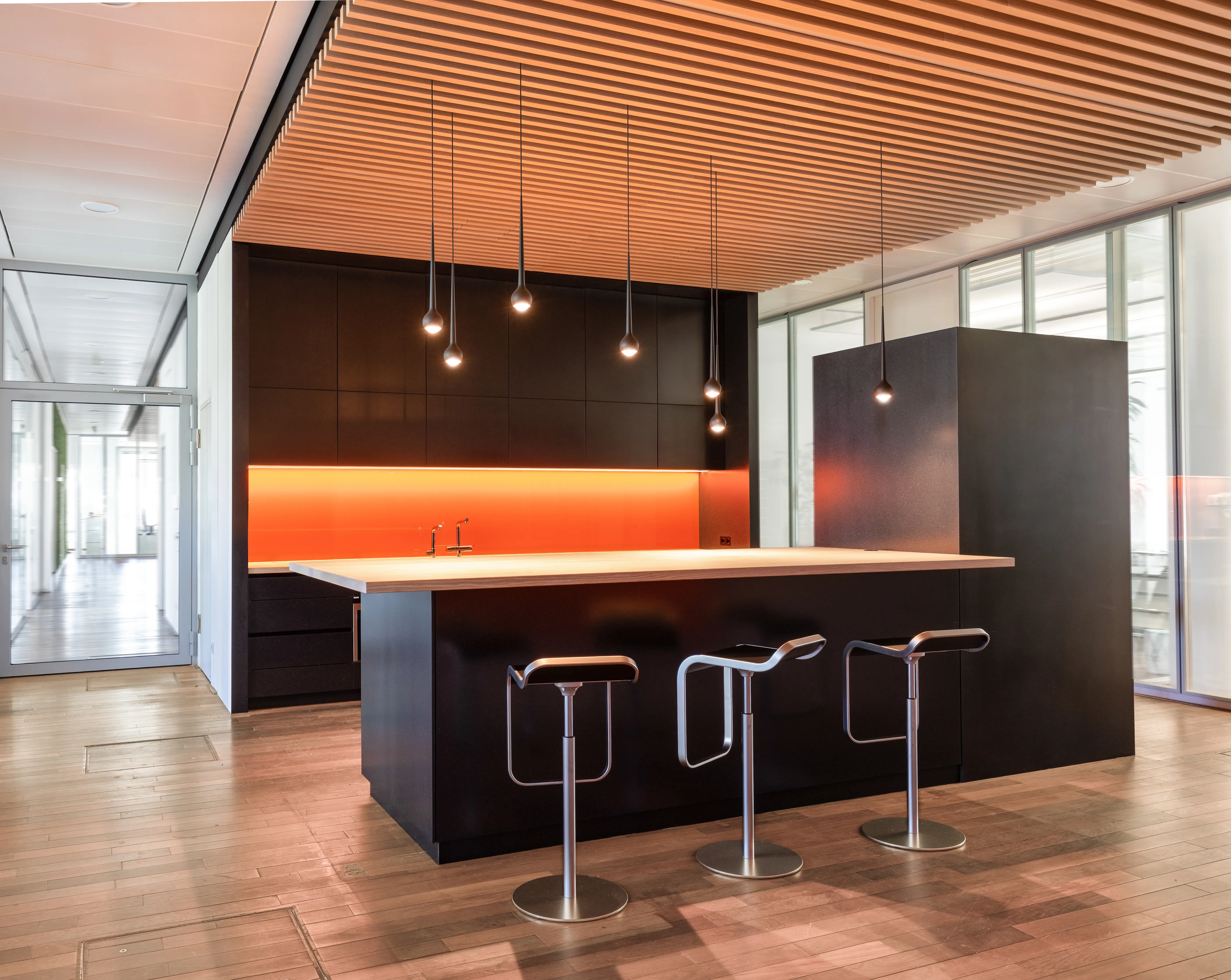A modern break area with a central black counter, bar stools, and warm wood accents.
