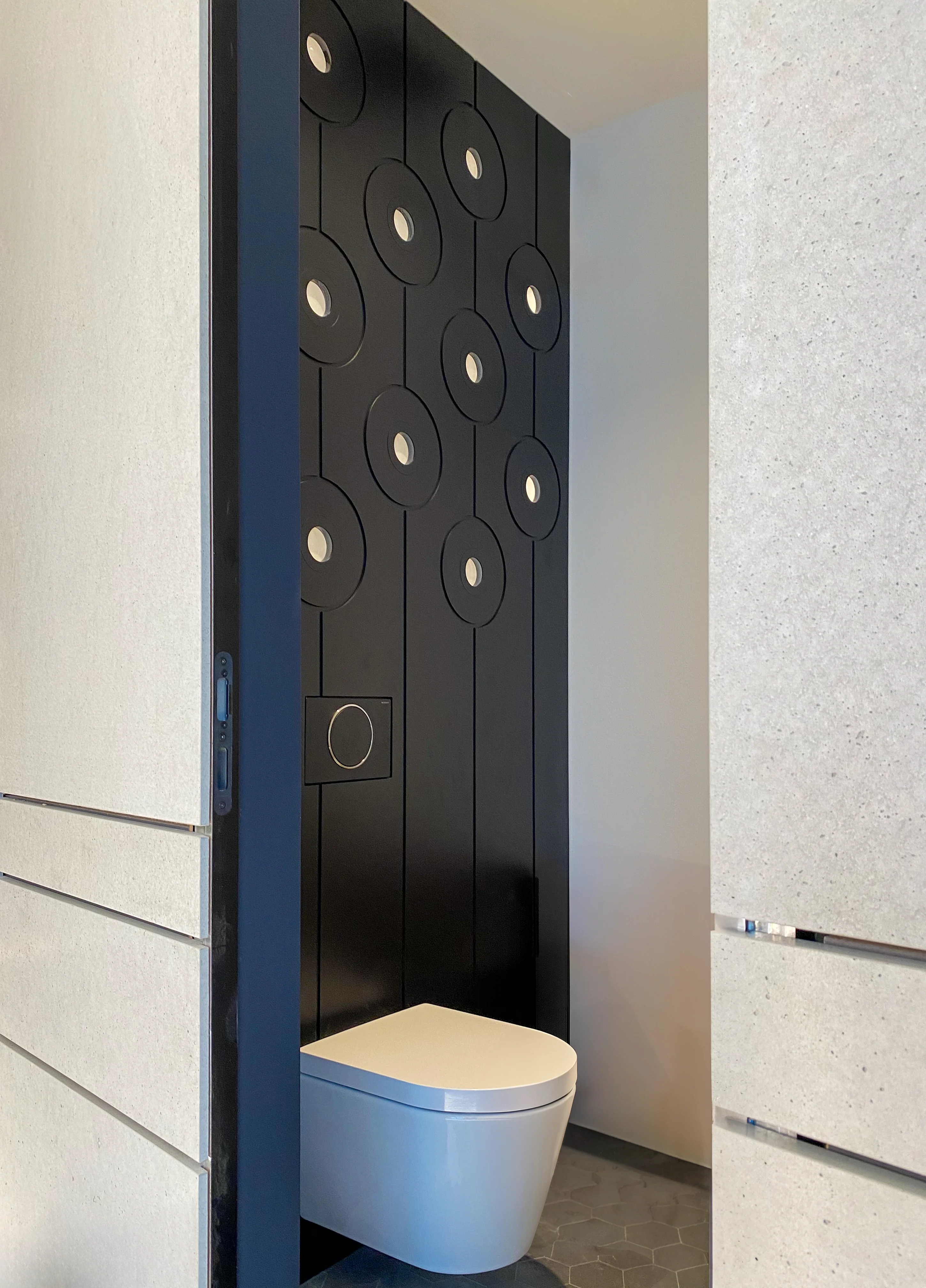 A minimalist restroom with dark walls, decorative lighting, and a white toilet.