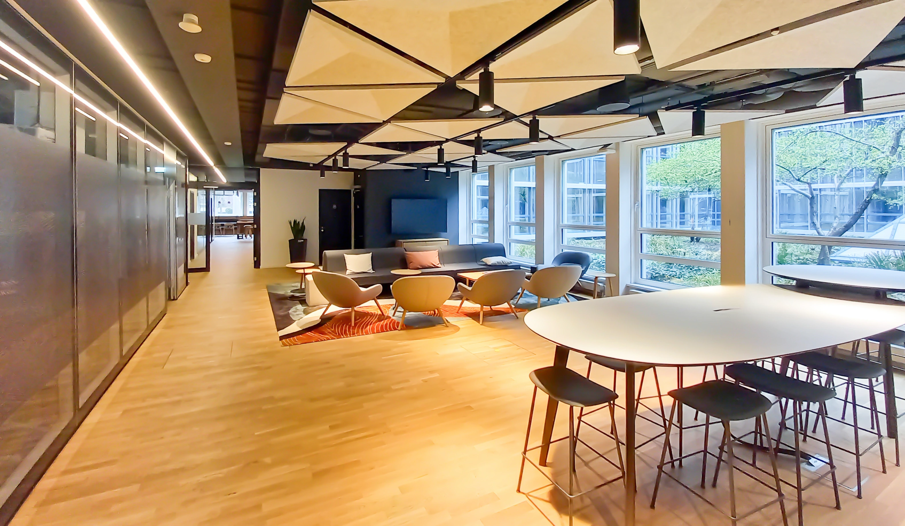 A spacious meeting space with wooden floors, exposed beams, and a mix of round and rectangular tables.