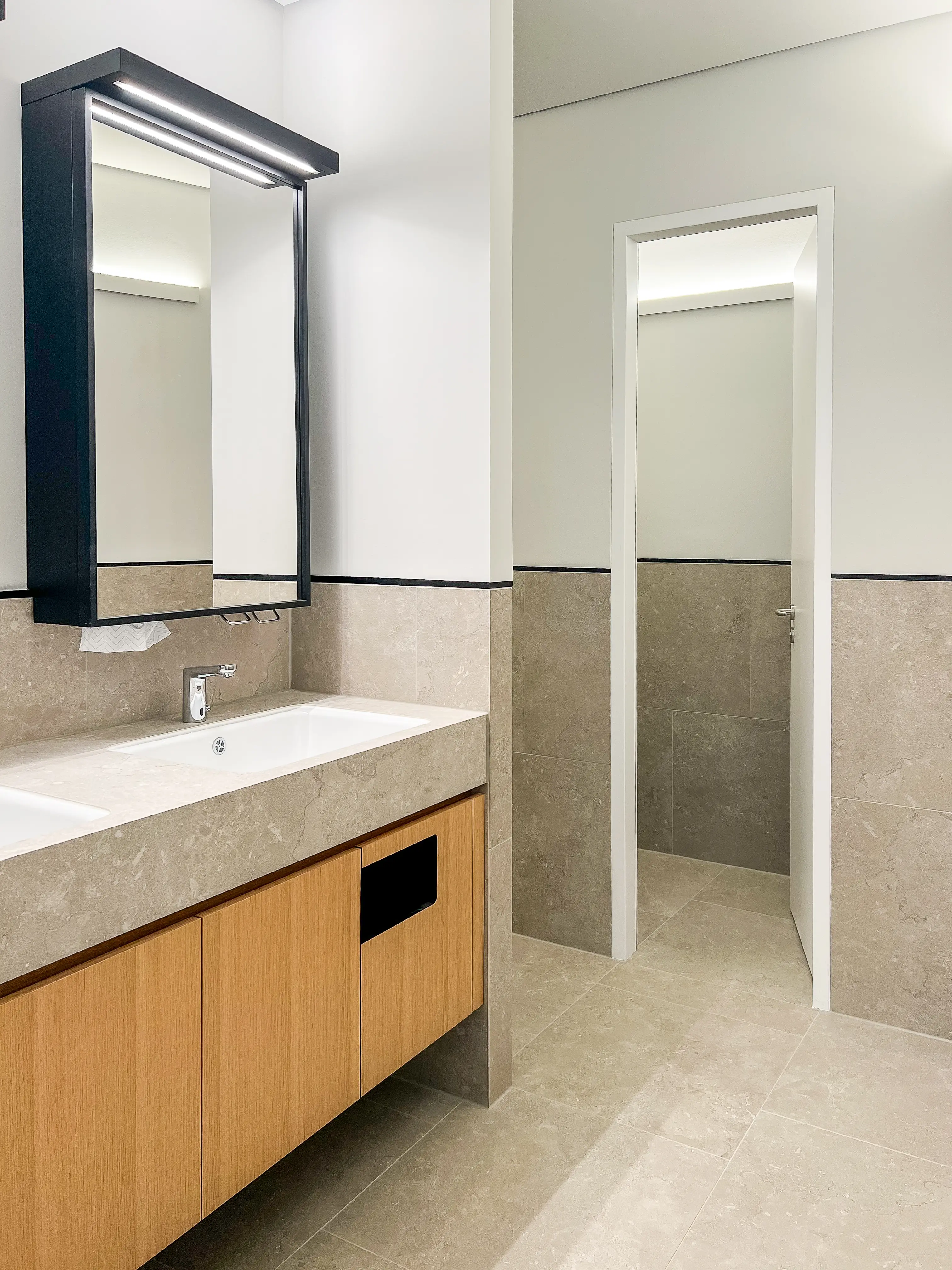 A modern restroom with a light wood vanity, large mirror, and minimalist fixtures.