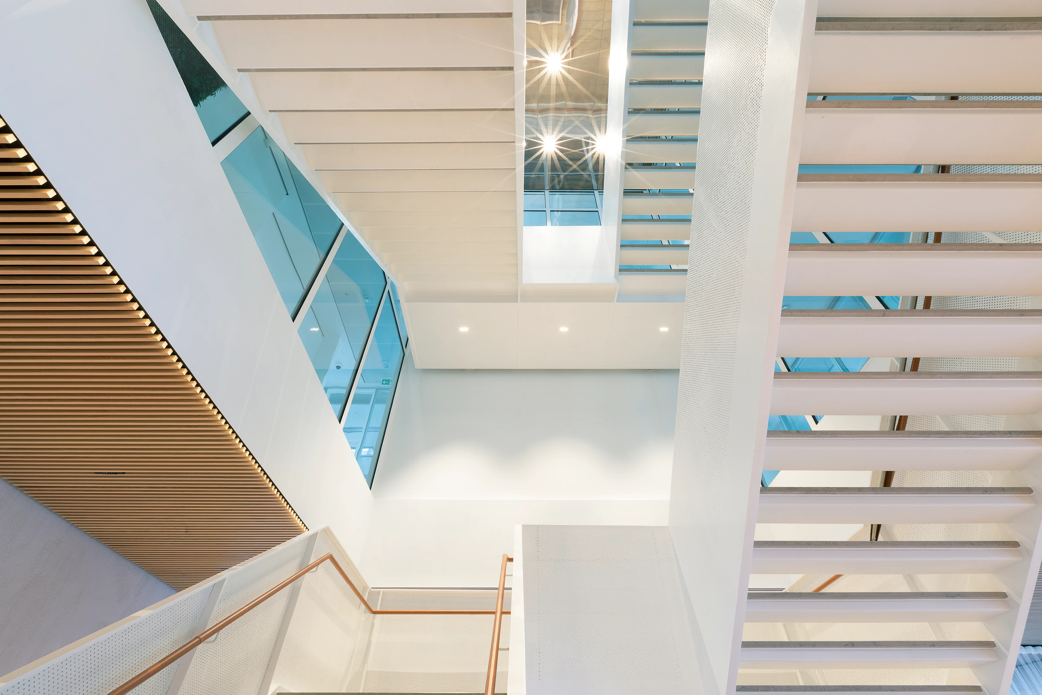 A minimalist staircase with white steps, wooden accents, and a glass railing illuminated by daylight.