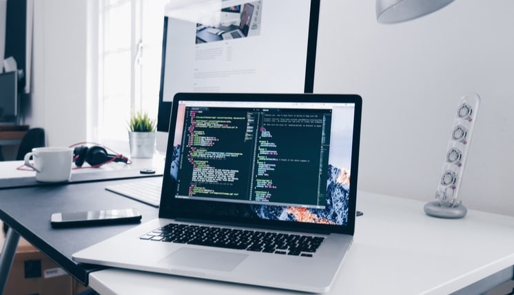 Laptop displaying code on screen placed on a clean desk with office items, representing software development or system design in a modern workspace.