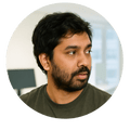 Profile photo of a man with short dark hair and beard, wearing a dark shirt, looking to the side in a modern office setting.