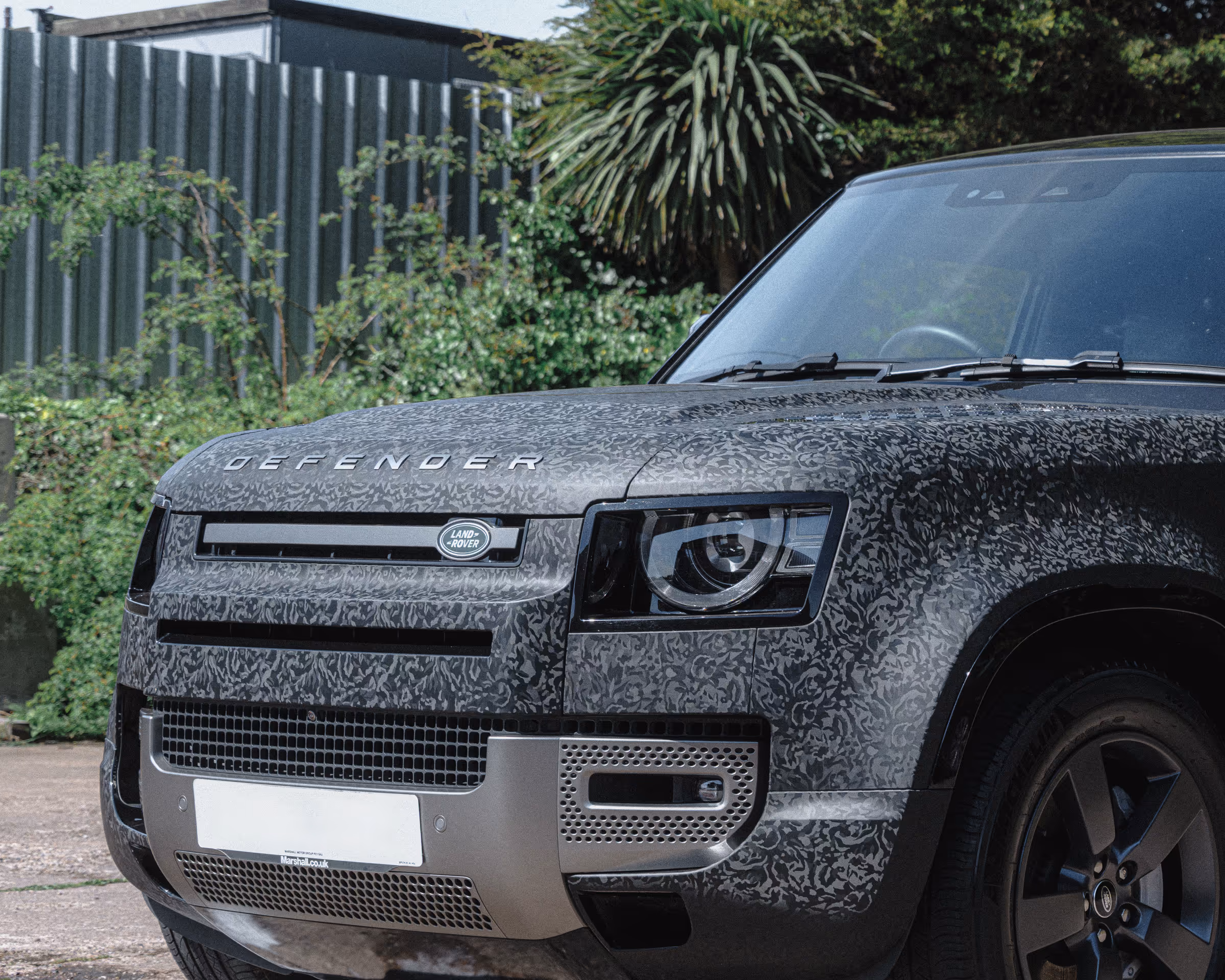 A Land Rover Defender 90 wrapped in a tactical black camo finish.