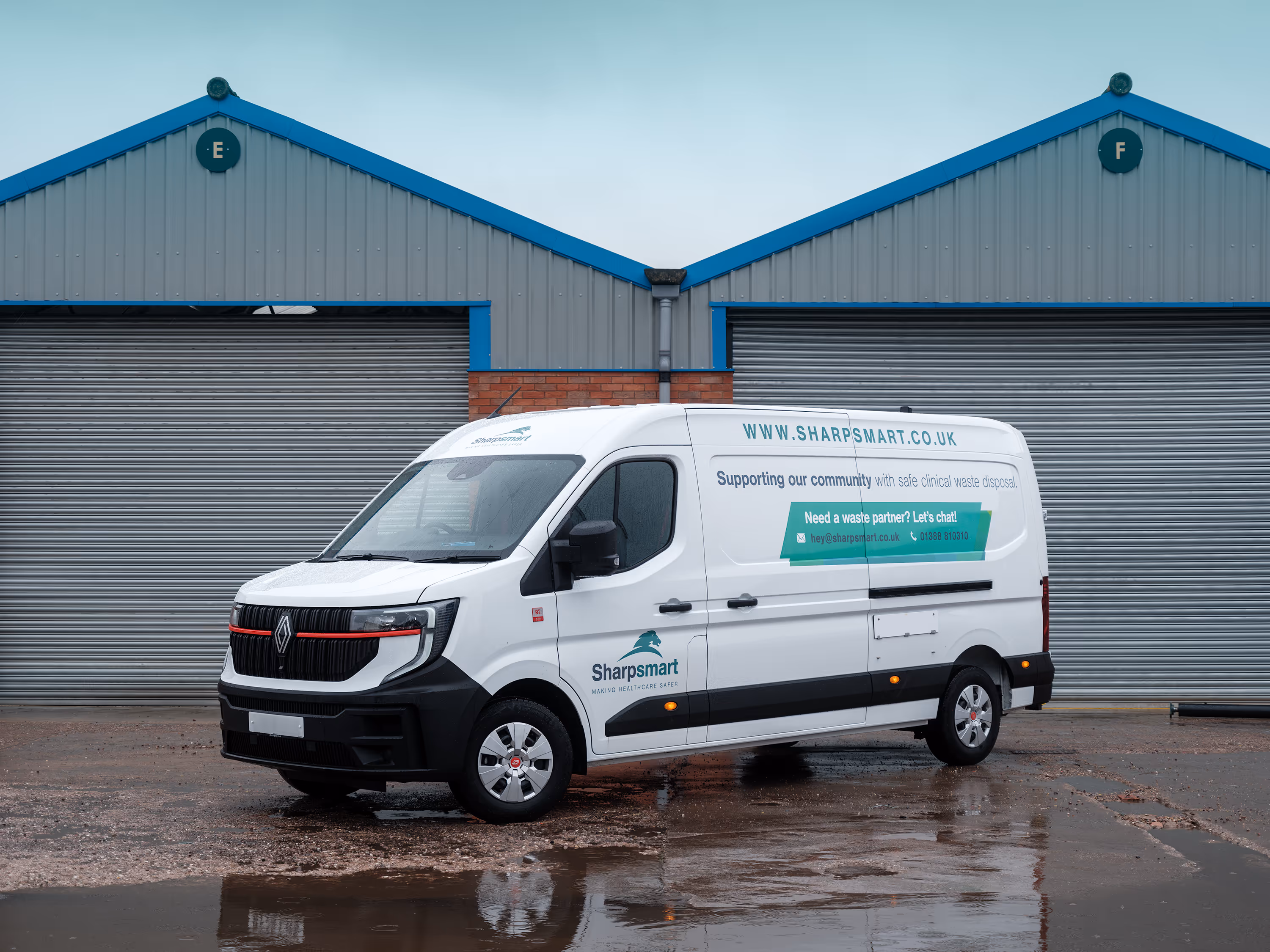 White Sharpsmart van parked on wet ground in front of two grey industrial roller doors.