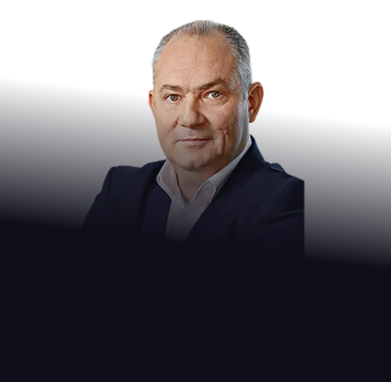 Middle-aged man with short gray hair wearing a dark blazer and white shirt, looking confidently forward against a dark background.