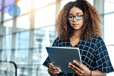 Woman with curly hair and glasses using a digital tablet in a bright modern office.
