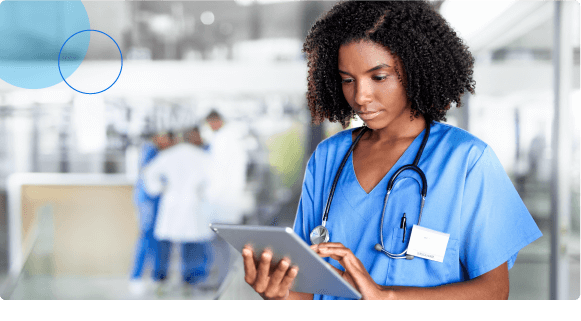 Female healthcare worker in blue scrubs using a digital tablet in a medical facility.
