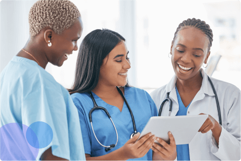 Three healthcare professionals smiling and looking at a tablet together in a bright clinical setting.