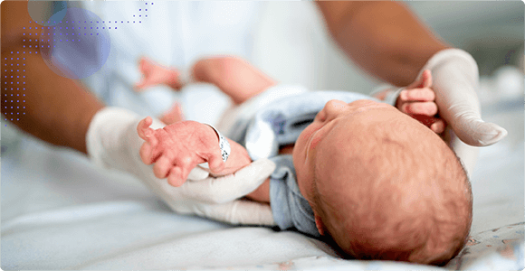 Newborn baby being gently held by gloved hands on a hospital bed.
