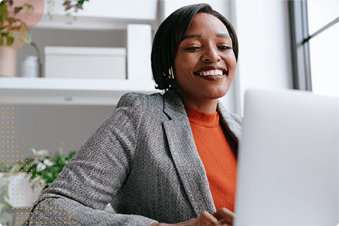 Smiling woman in gray blazer working on a laptop in a modern home office.