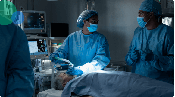 Medical team in scrubs and masks administering anesthesia to patient in operating room.